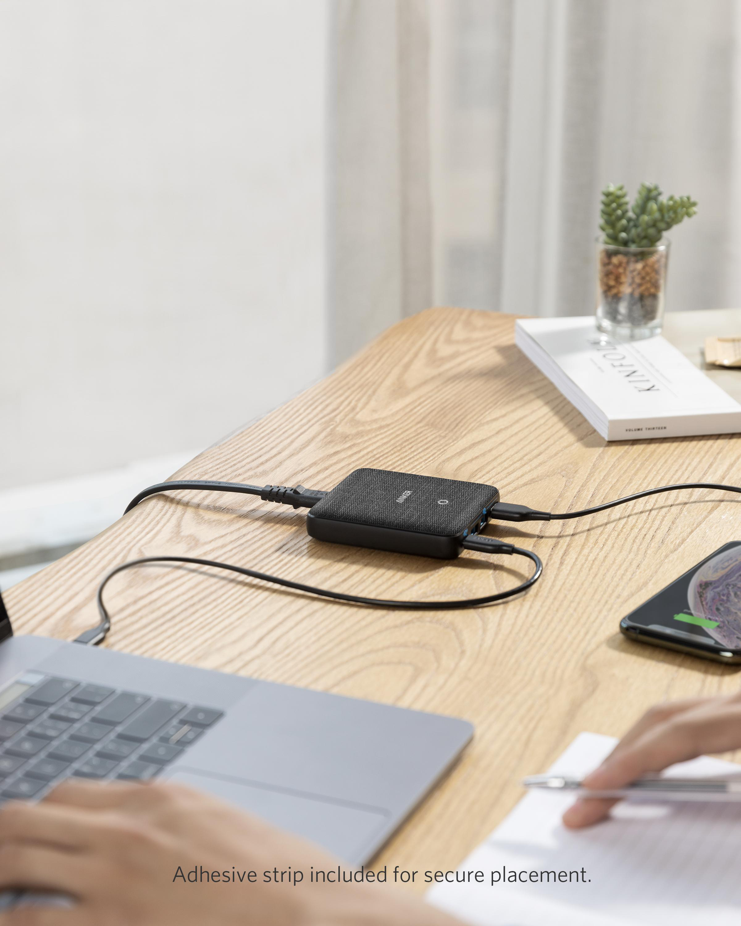 Schwarzer Hub mit Kabeln auf einem Holztisch, Laptop und Telefon in der Nähe.