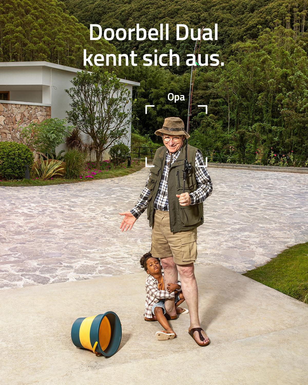 Ein älterer Mann mit Hut und Angelrute steht neben einem Kind, das sich an sein Bein klammert.