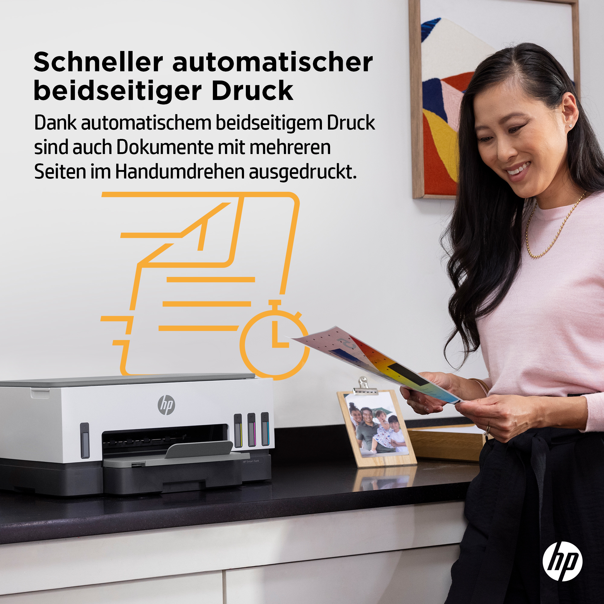 Frau lächelt einen Drucker auf einem Schreibtisch mit farbigem Papier, einem Fotorahmen und Text an.