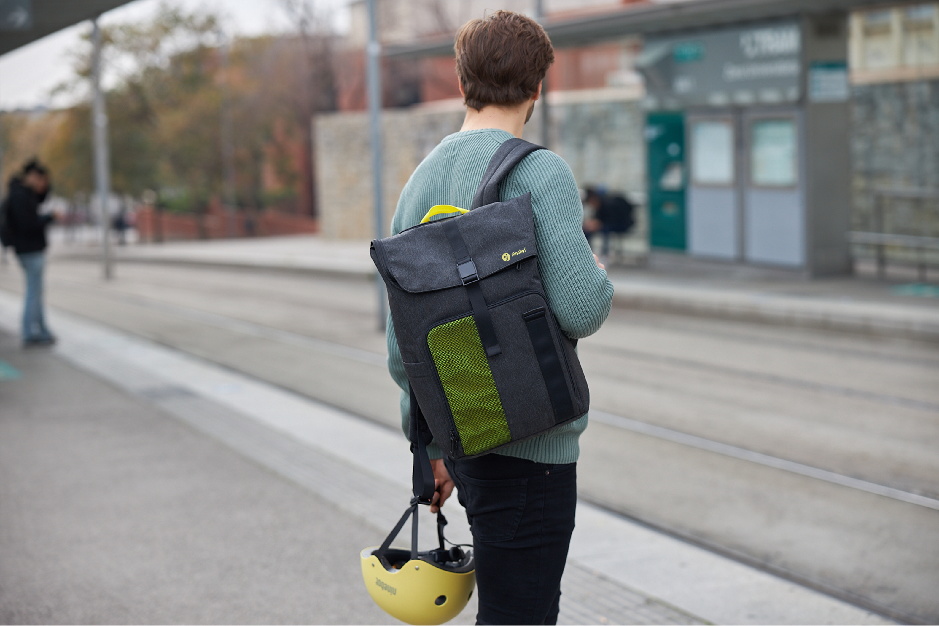Eine Person mit Rucksack geht auf einer Straße in der Nähe einer Bushaltestelle.
