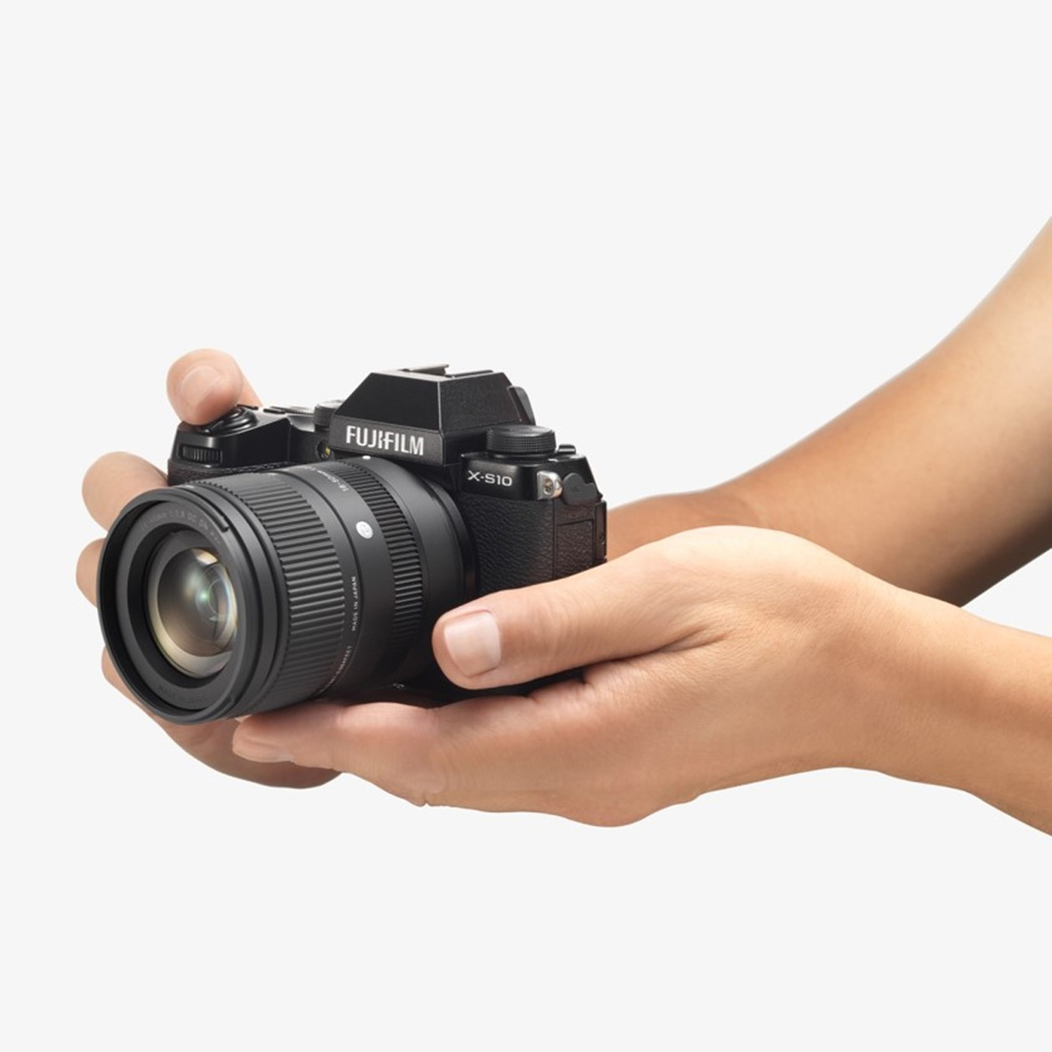 Una persona tiene in mano una fotocamera FujiFilm nera con obiettivo. Mani visibili.