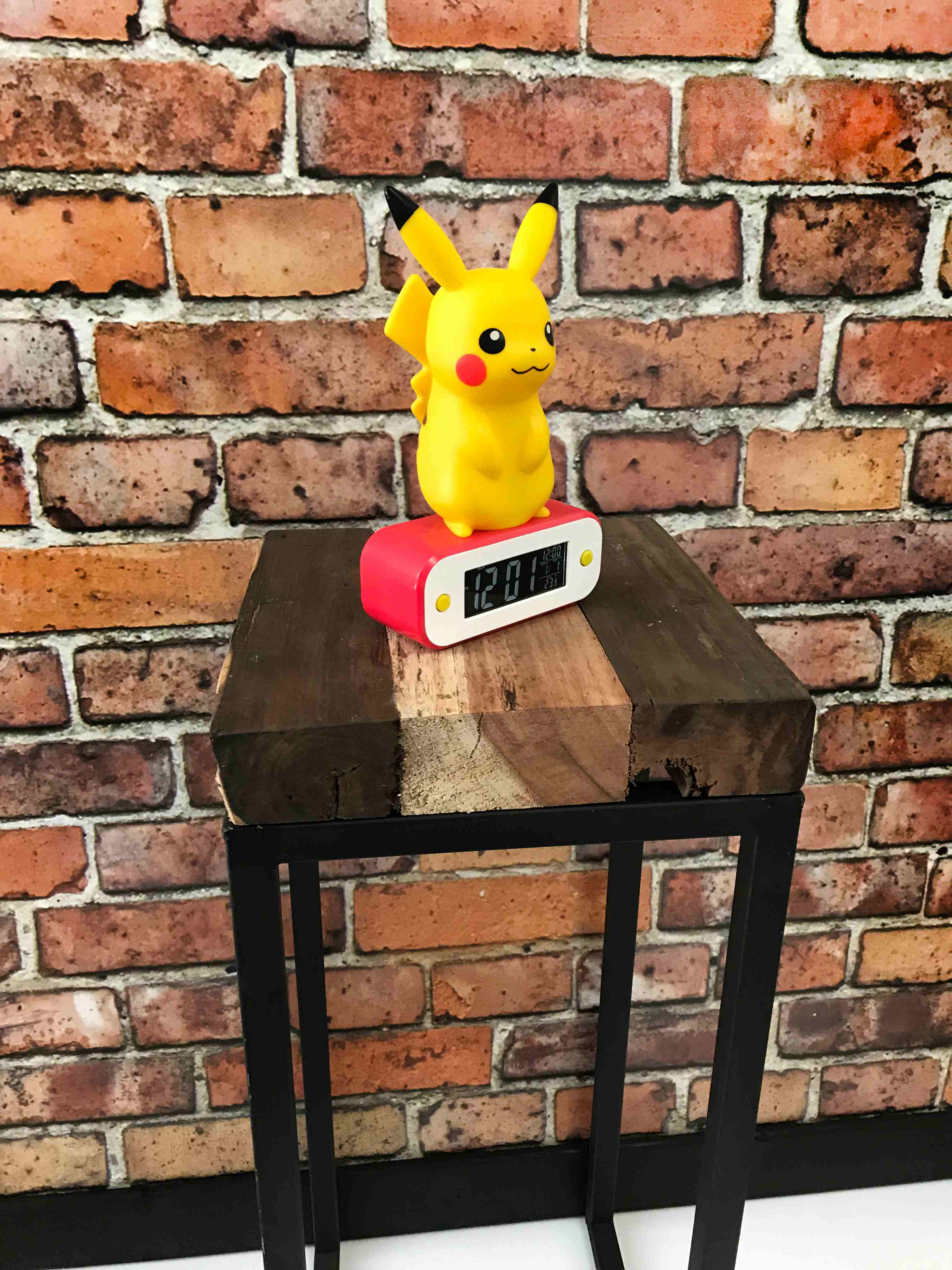 Sveglia di Pikachu su un tavolo di legno con sfondo in mattoni, primo piano.