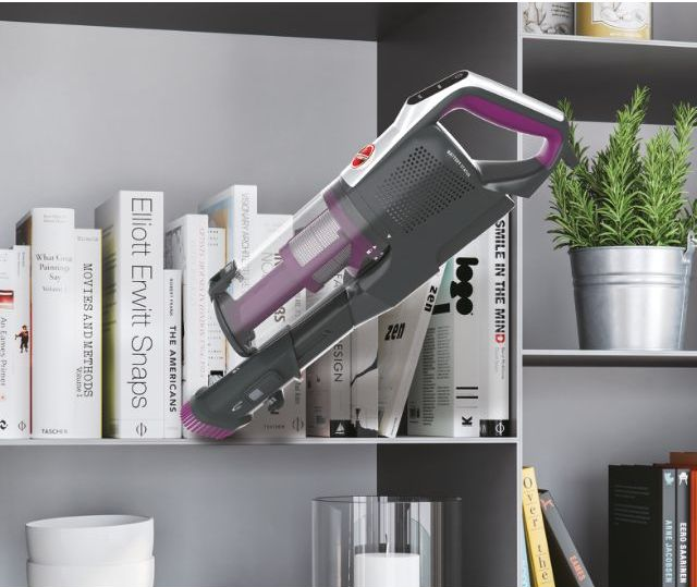 Un aspirateur à main noir et violet est sur une étagère avec des livres et d'autres objets.