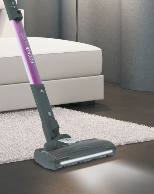 Aspirateur Hoover avec une poignée violette sur un tapis clair et un sol en bois.