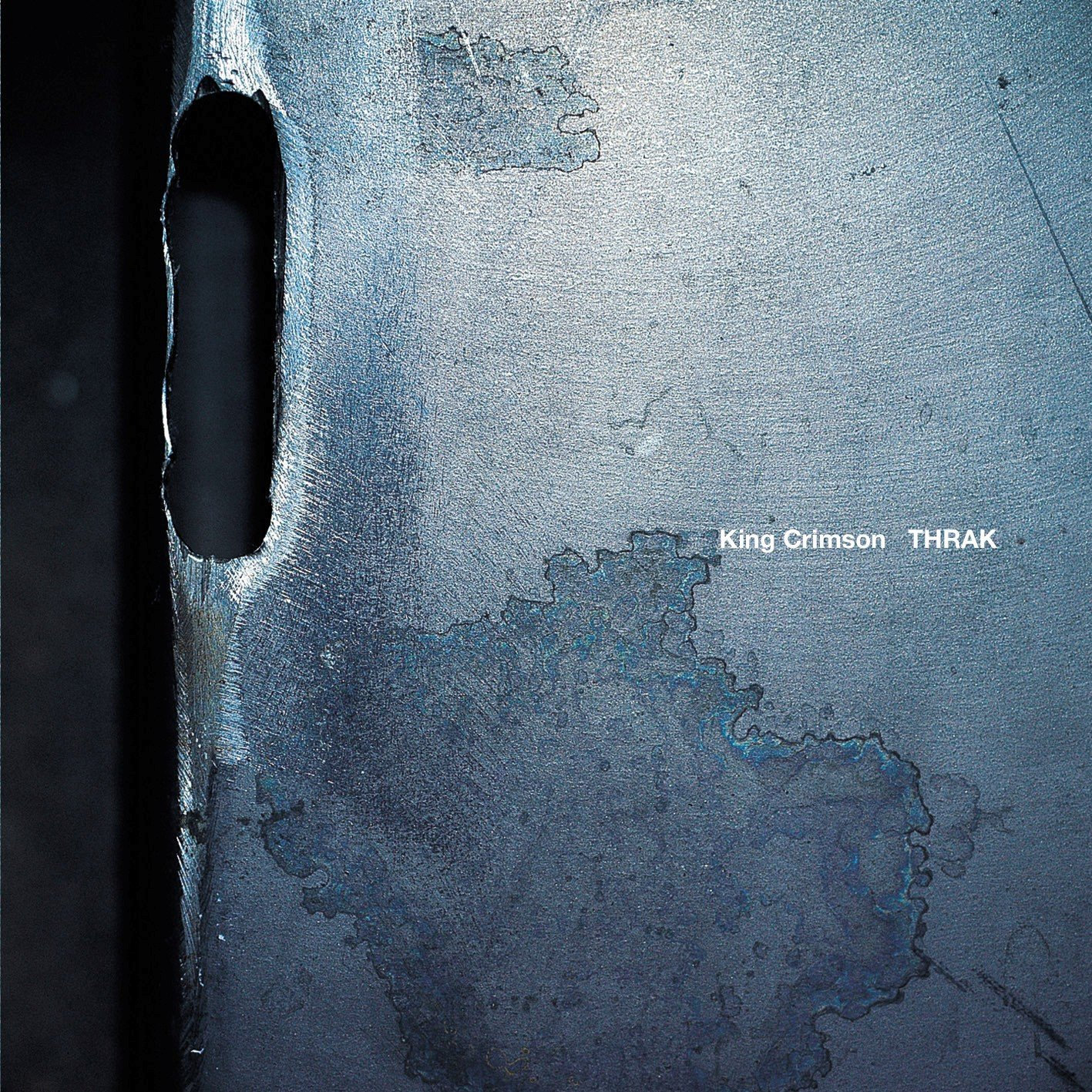 Absztrakt fémfelület a King Crimson 'THRAK' album borítójával. A felület texturált, kopottas.