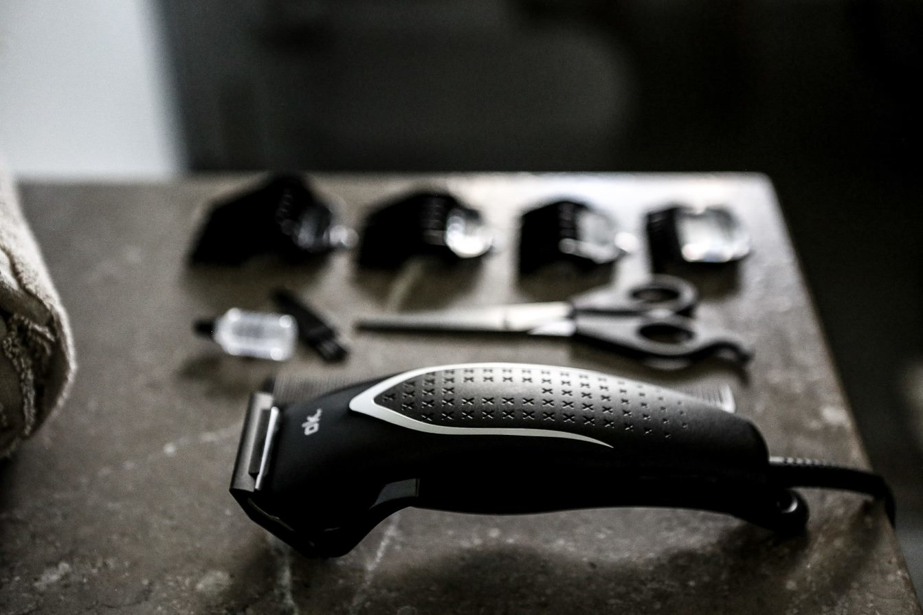 A black hair clipper with attachments and scissors on a gray surface.