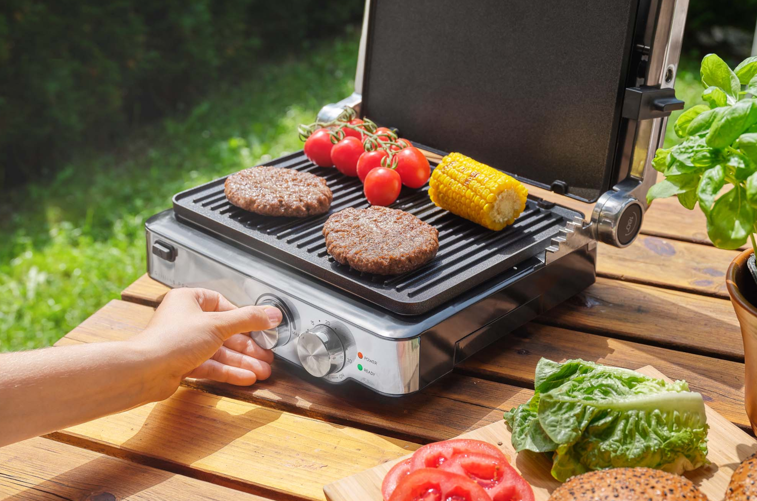 Grill hamburgerekkel, paradicsommal és kukoricával, kézzel állítva a tárcsát.