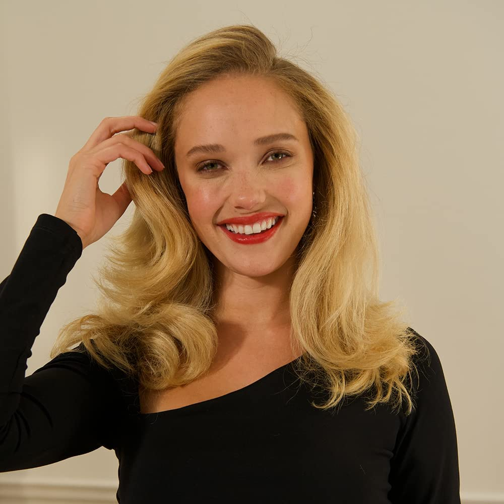 Blonde Frau lächelt, mit rotem Lippenstift und welligem Haar, blickt in die Kamera. Schwarzes Oberteil.