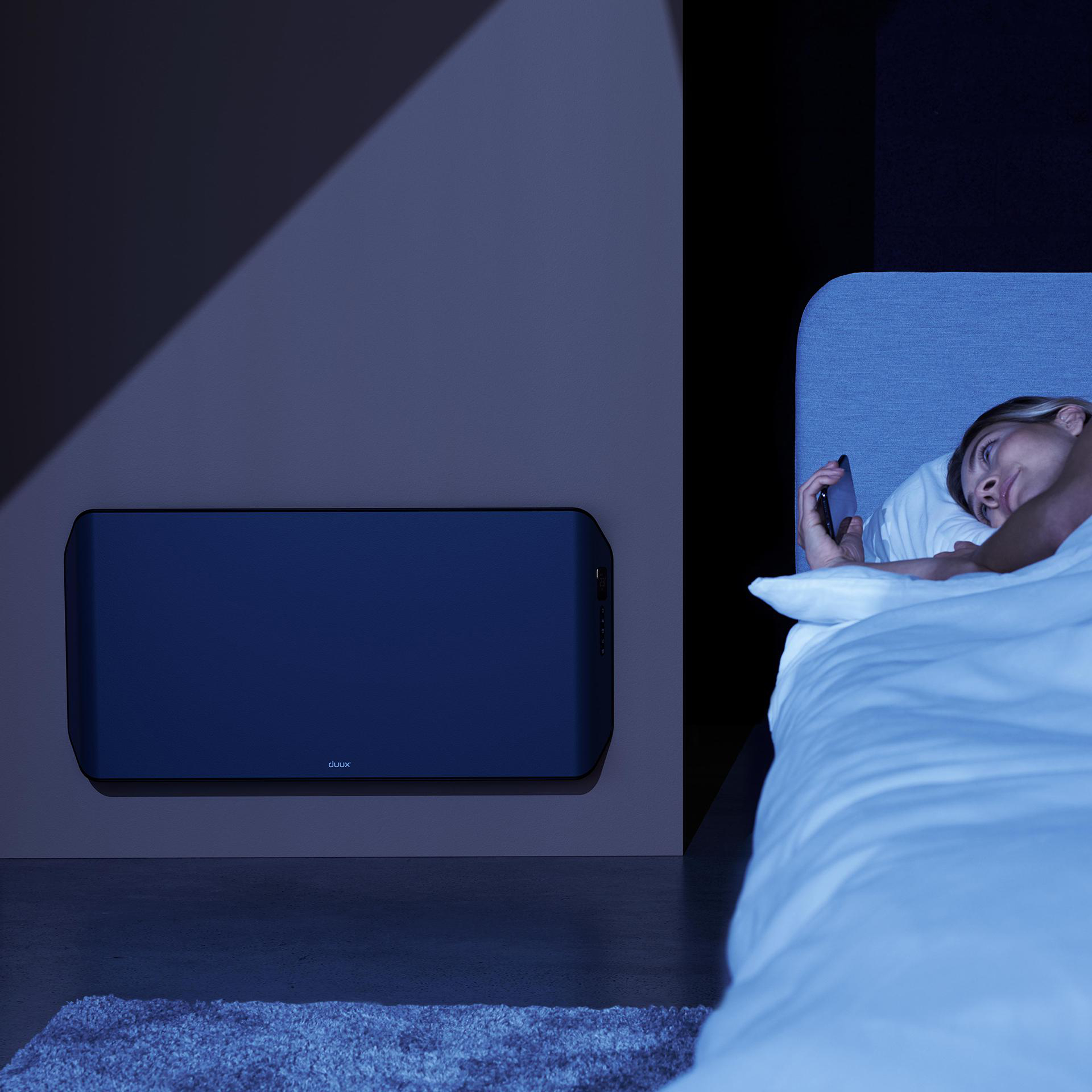 Eine Frau im Bett, die auf ein Telefon schaut, mit einem Wandheizkörper an der Wand.