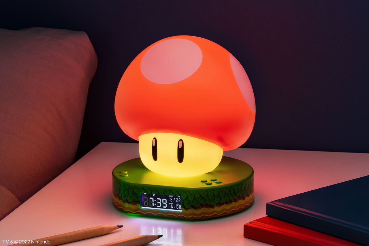 Ein Super Mario Pilz-Wecker auf einem Nachttisch mit Bleistiften und Büchern.