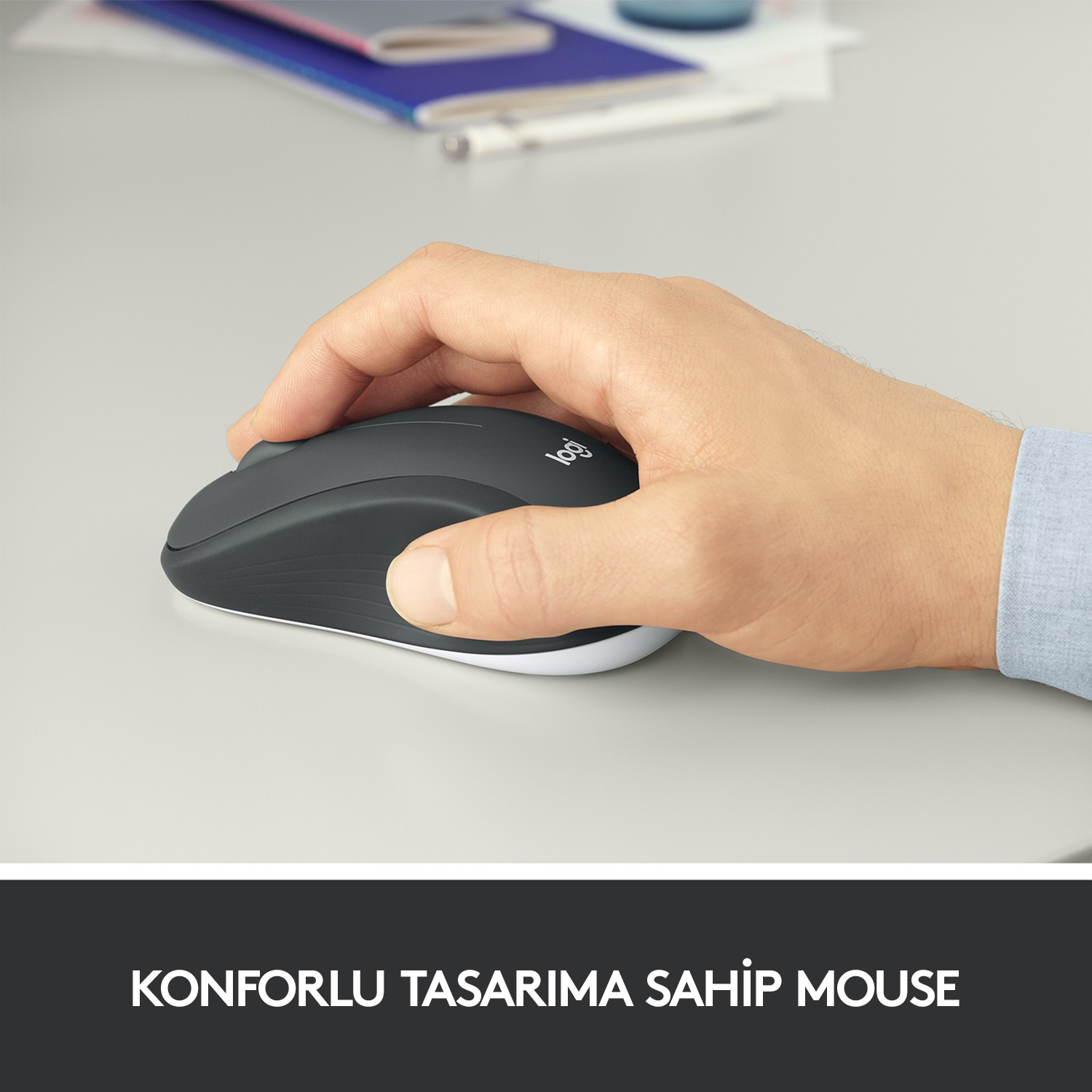 Açık gri bir yüzeyde, koyu gri bir Logitech fare tutan bir el.