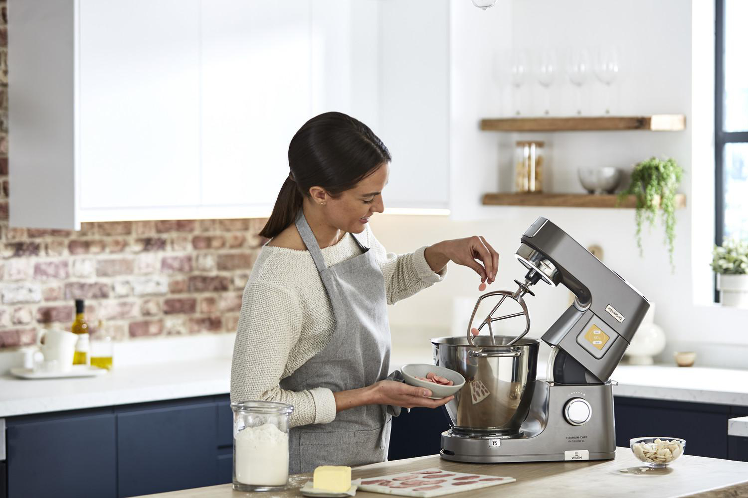 Eine Frau benutzt eine Kenwood Küchenmaschine in einer Küche. Zutaten sind auf der Theke.