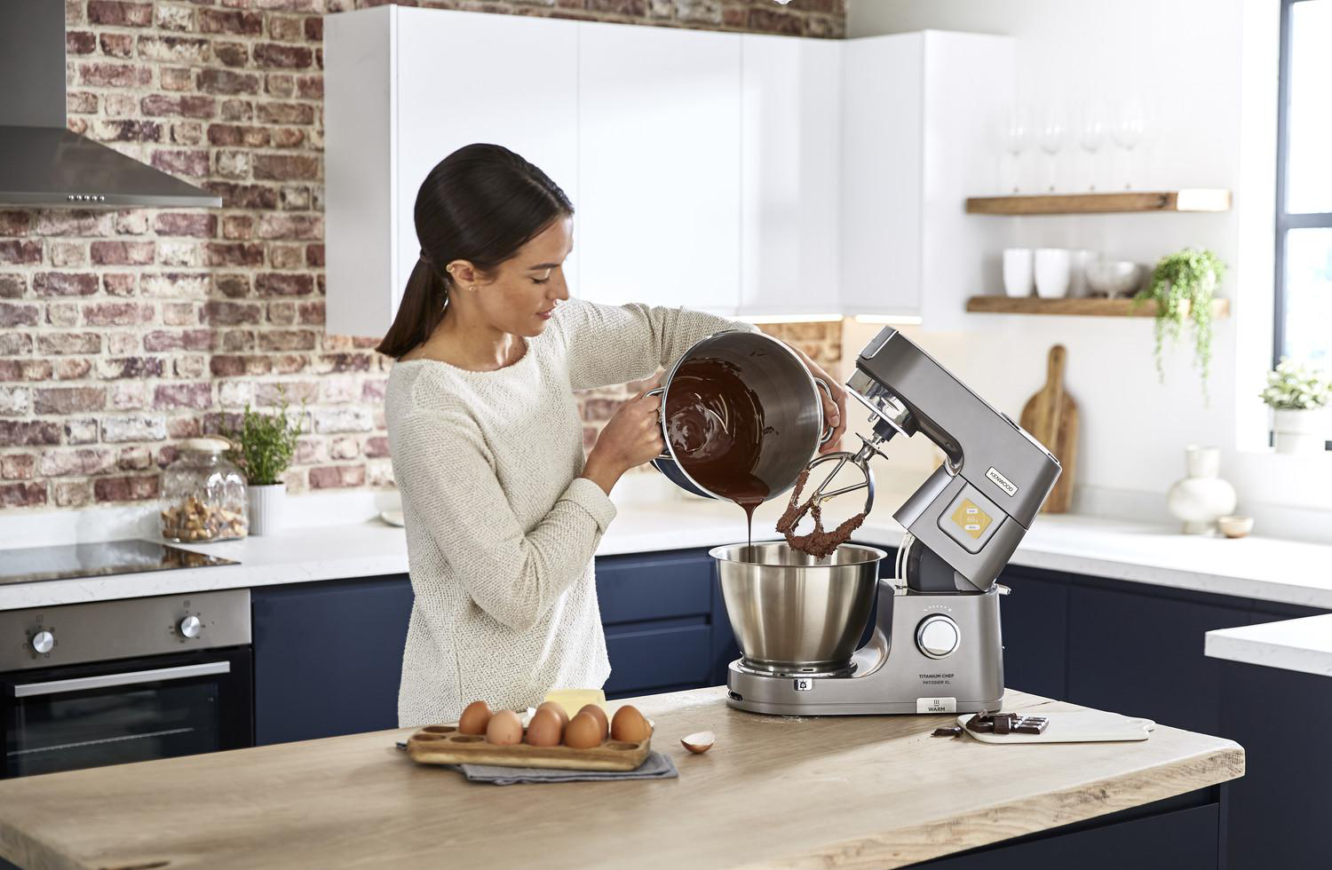 Eine Frau gießt Schokoladen-Teig in einen Mixer, mit Eiern und Butter auf der Theke.