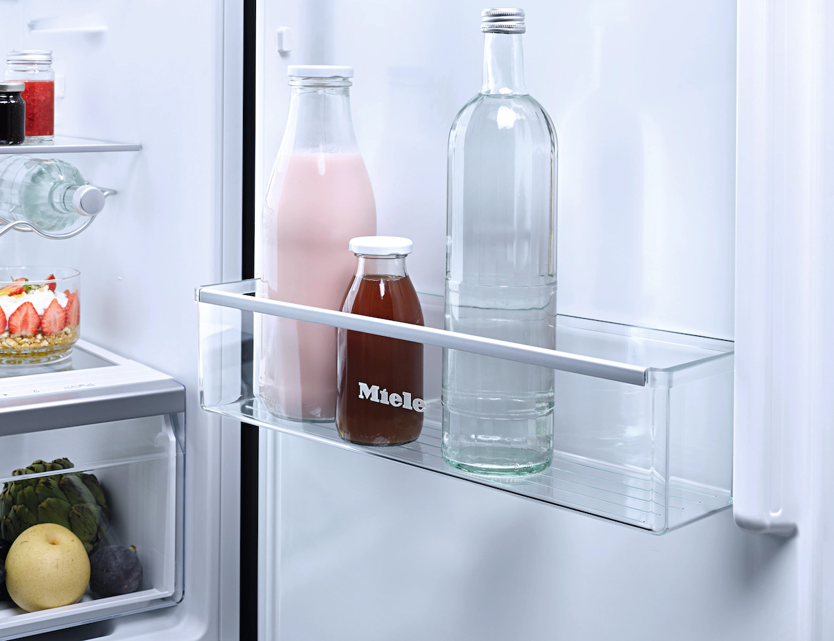 Kühlschrankregal mit Glasflaschen Milch und Wasser. Es gibt eine kleine 'Miele'-Flasche.