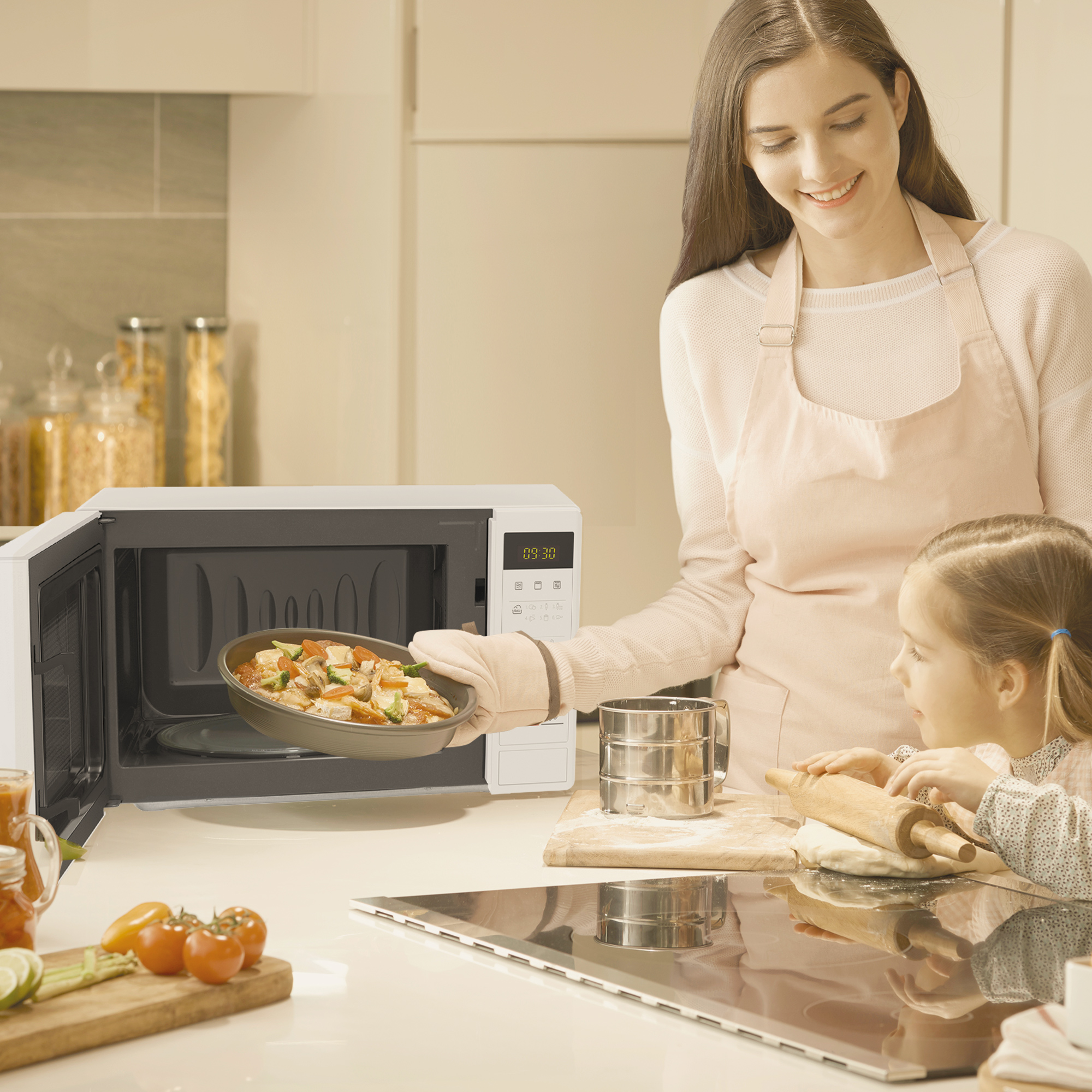 Una mujer y una niña en una cocina. La mujer sostiene una bandeja con comida frente a un microondas.