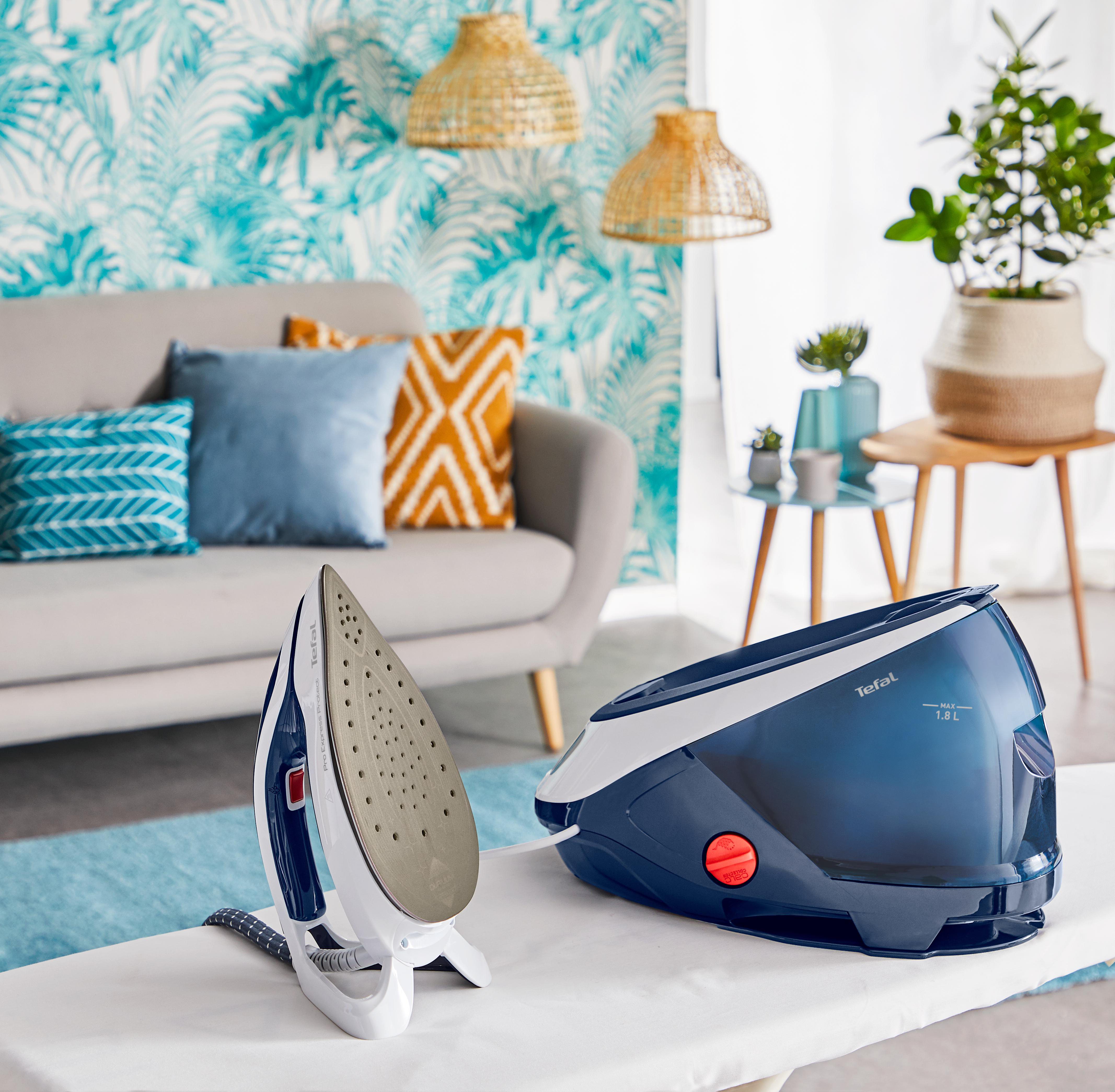 Ein Bügeleisen und ein Dampfgenerator stehen auf einer weißen Oberfläche, im Hintergrund eine graue Couch.