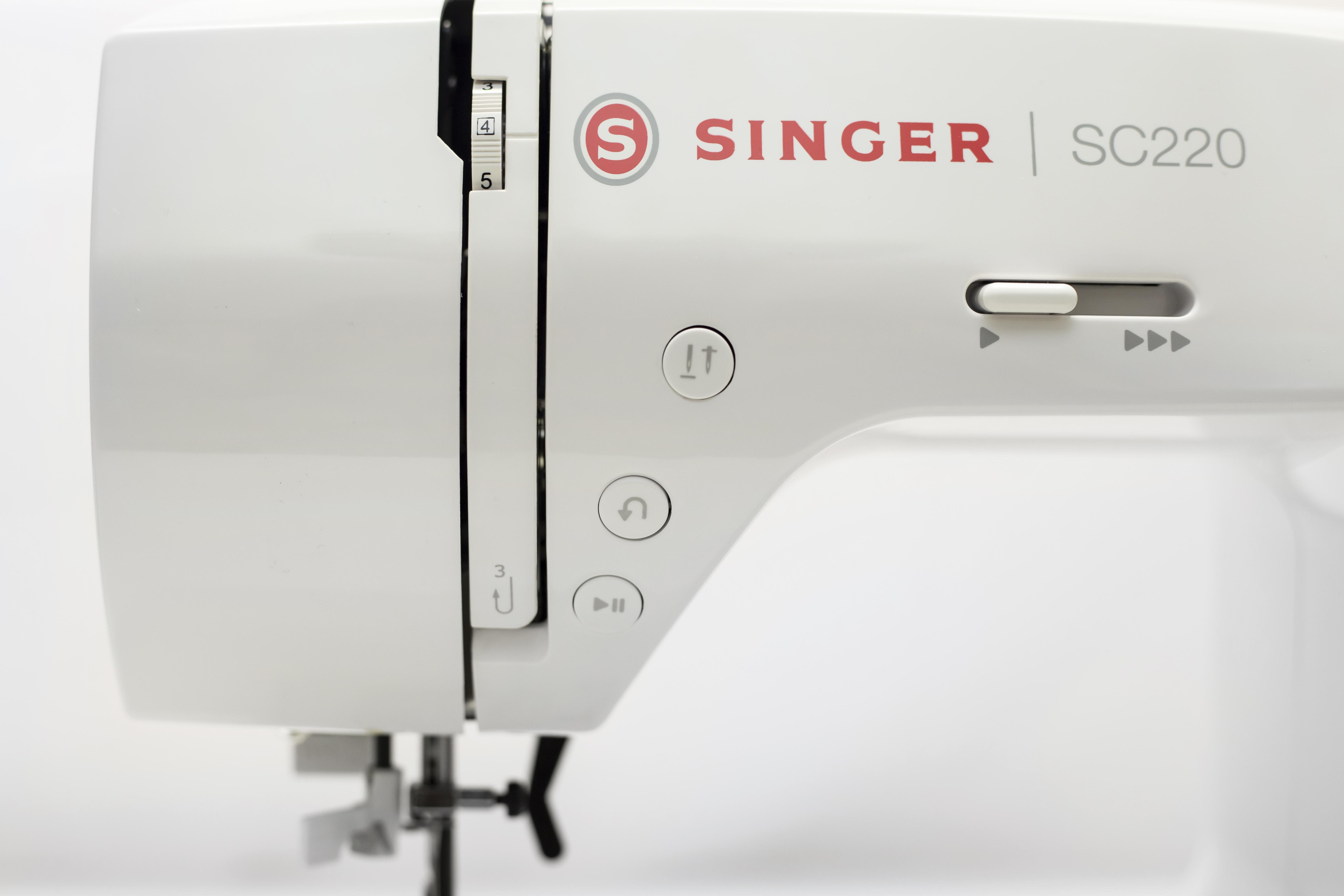 Nahaufnahme einer Singer-Nähmaschine. Weiße Maschine, rotes Singer-Logo. Bedienelemente und Knöpfe sichtbar.