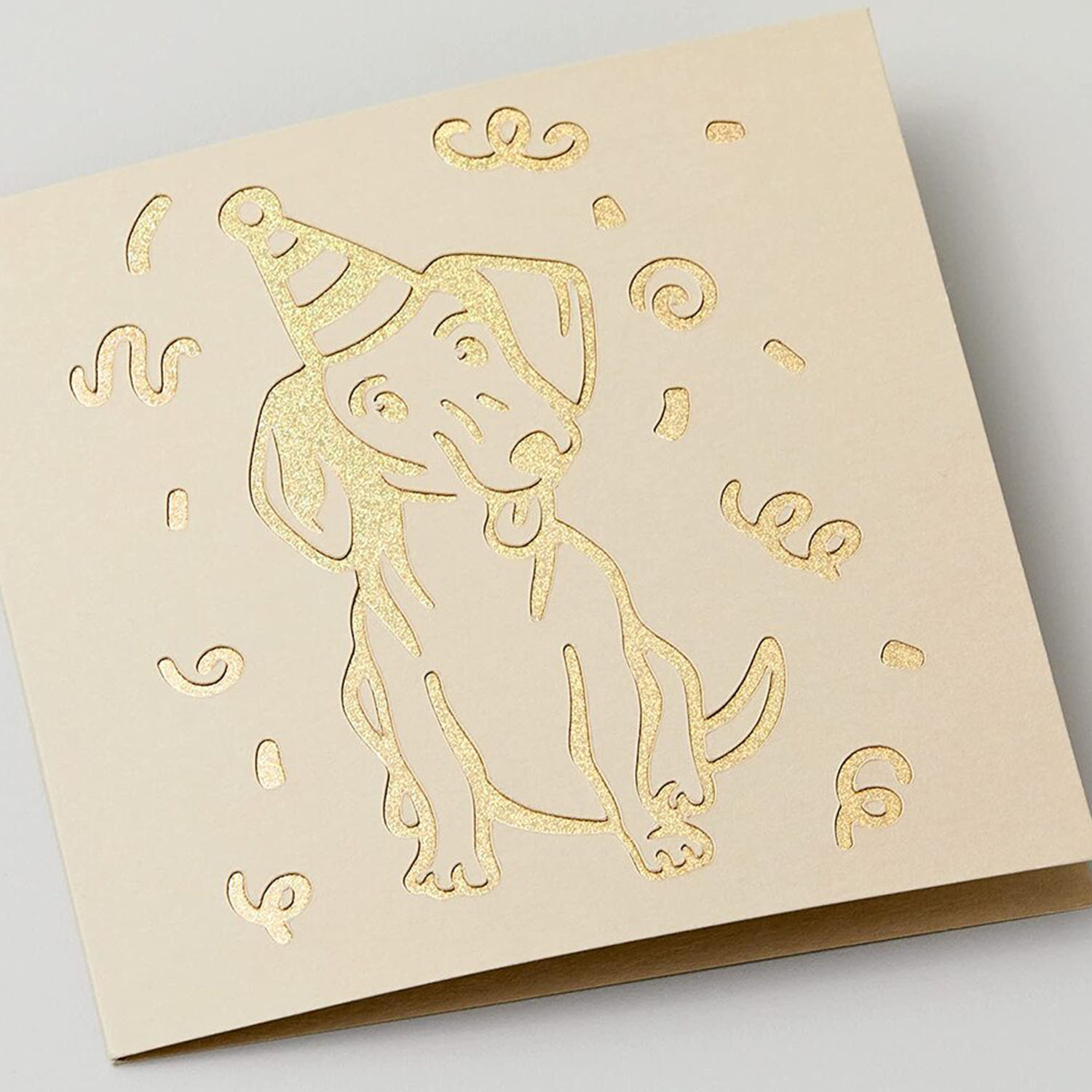 Biglietto di auguri con un cane bassotto dorato con cappello da festa e disegno di coriandoli.