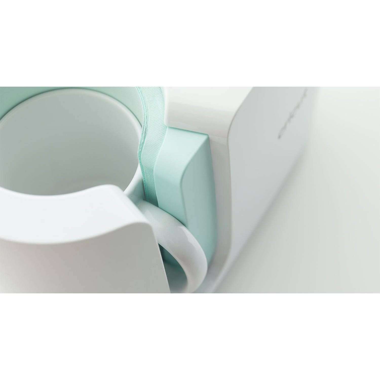Erogatore di nastro adesivo bianco e verde acqua con tazza da caffè bianca. Messa a fuoco sulla tazza e sul bordo del nastro.