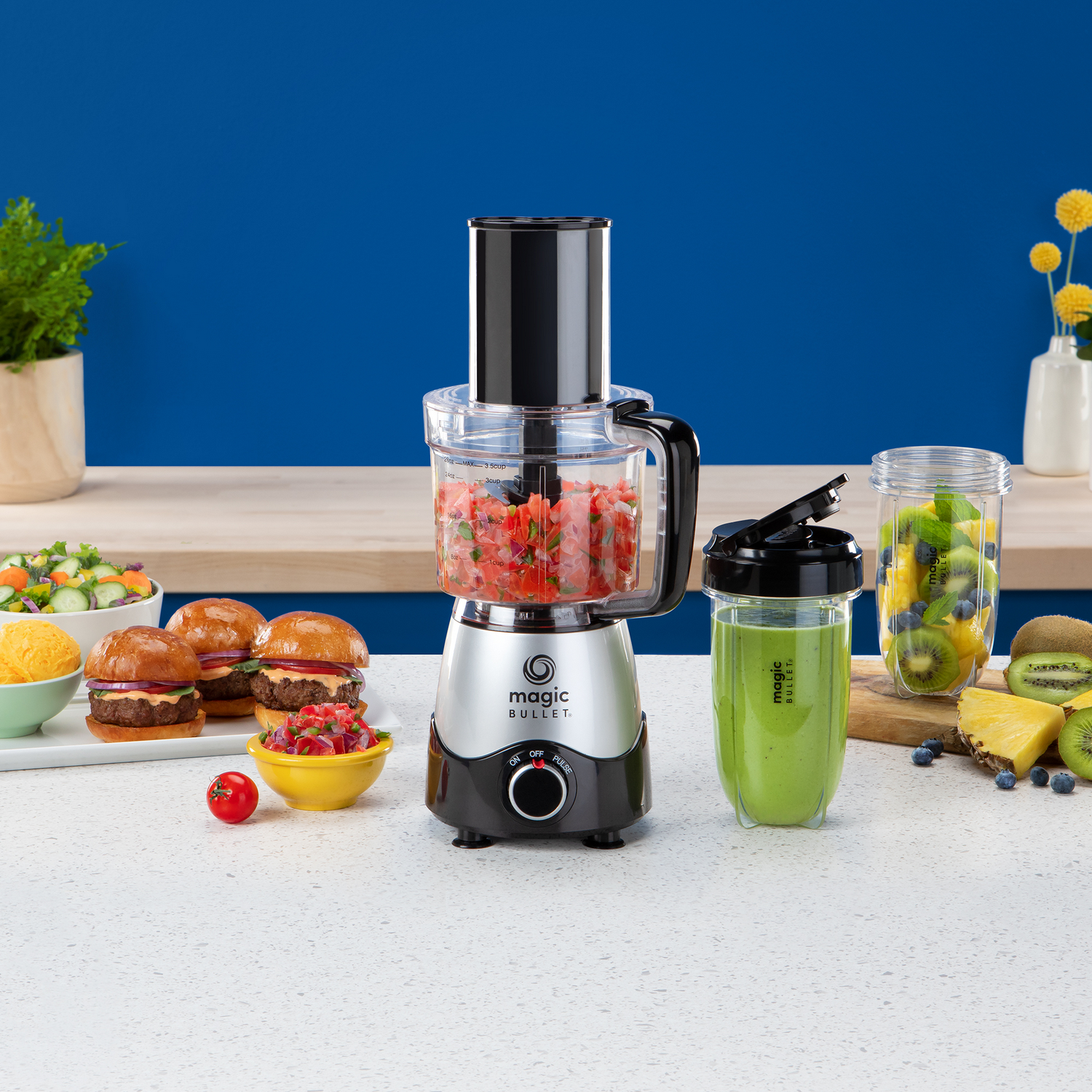 Magic Bullet keukenmachine met ingrediënten: burger, salade, kiwi. Blauwe achtergrond, wit aanrecht.