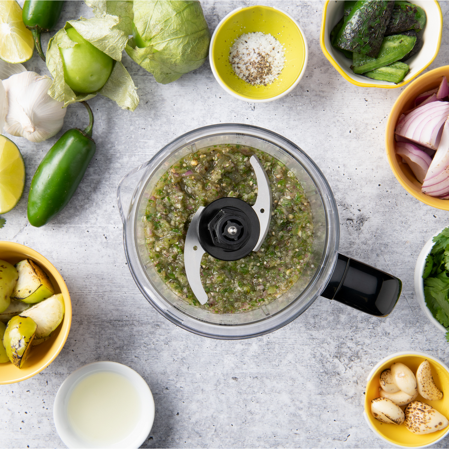 Keukenmachine met salsa-ingrediënten. Groene salsa, ingrediënten in gele kommen.