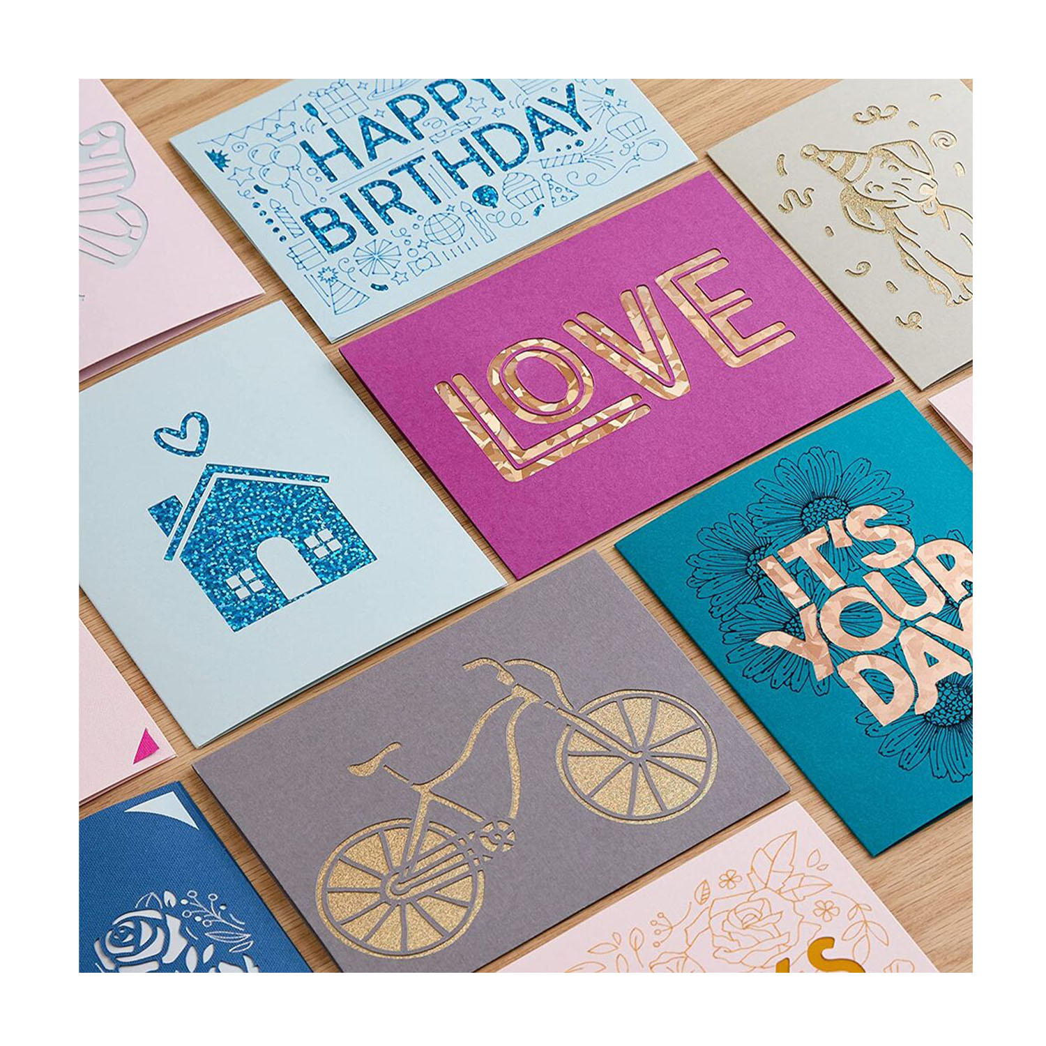 Varie biglietti di auguri colorati, alcuni con scritte dorate, disposti su legno.