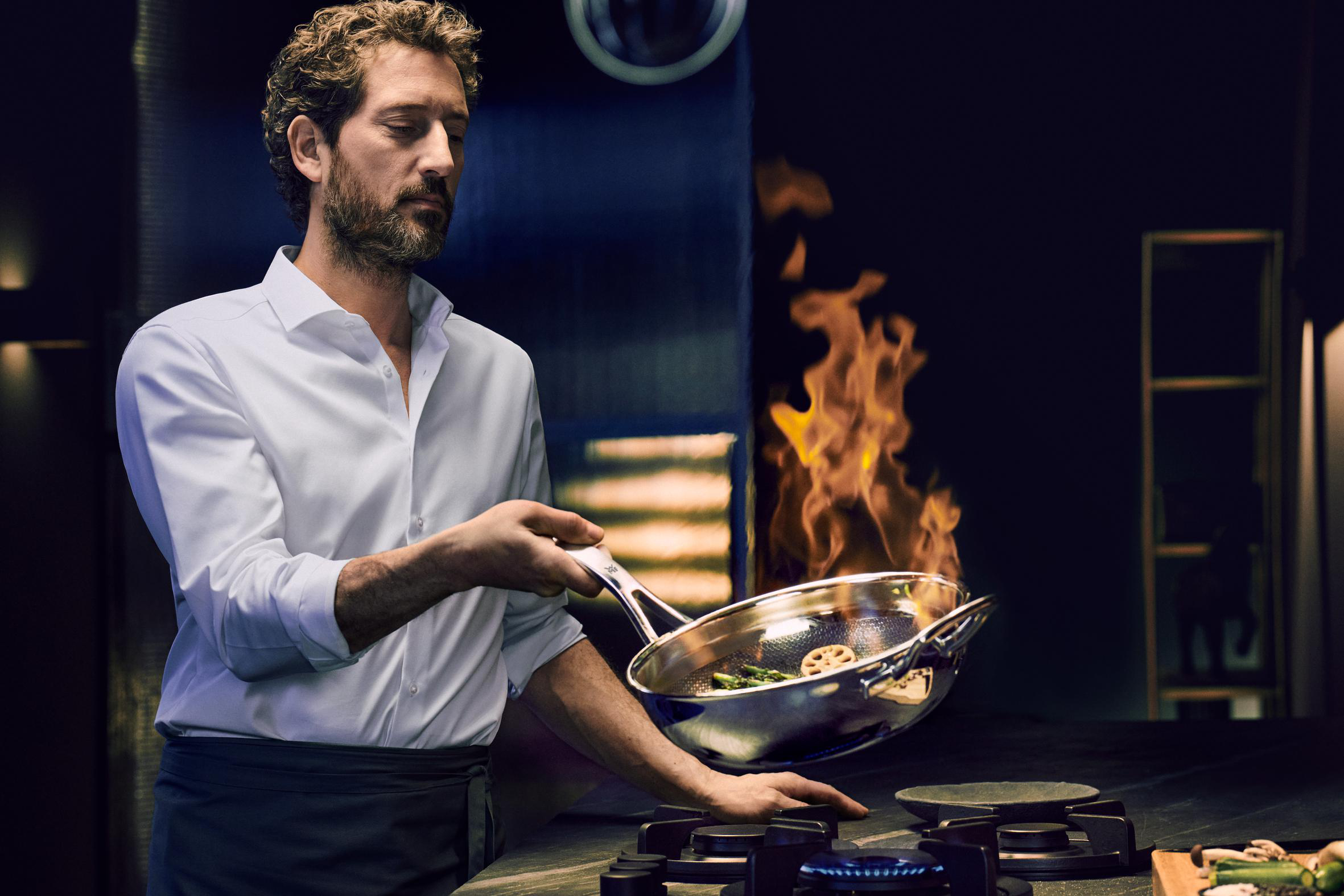 Ein Koch wirft Essen in einer Pfanne über einem Herd, mit Flammen.