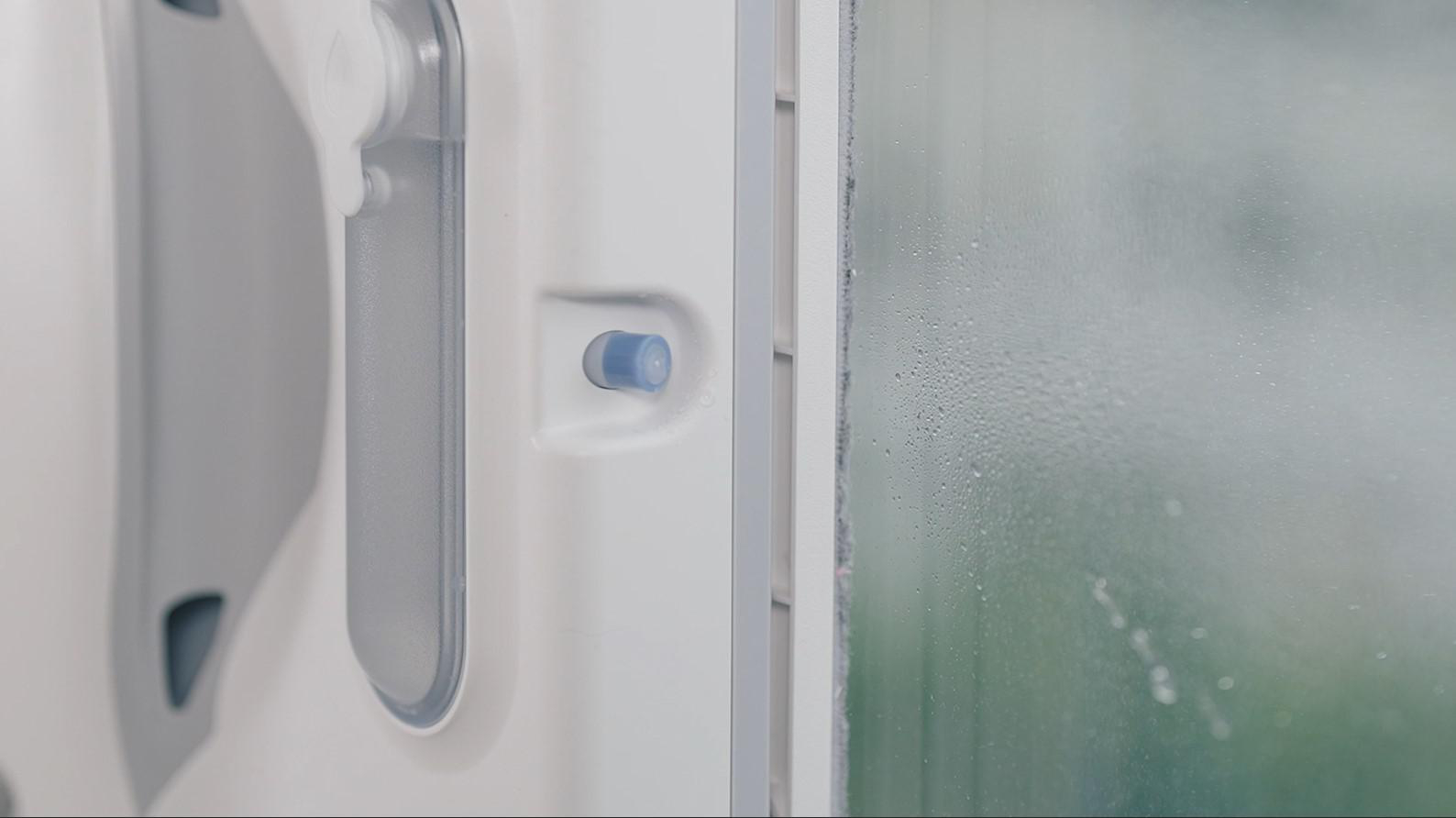 Fensterreinigungsgerät an einem Fenster, Tropfen sichtbar.