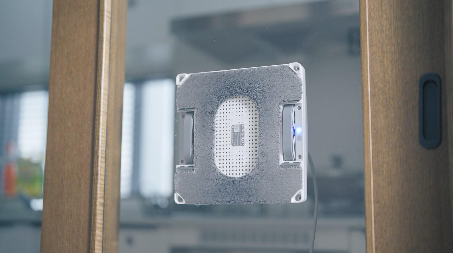 Ein Fensterputzroboter an einer Glasscheibe. Der Roboter ist weiß und hat ein graues Reinigungspad.