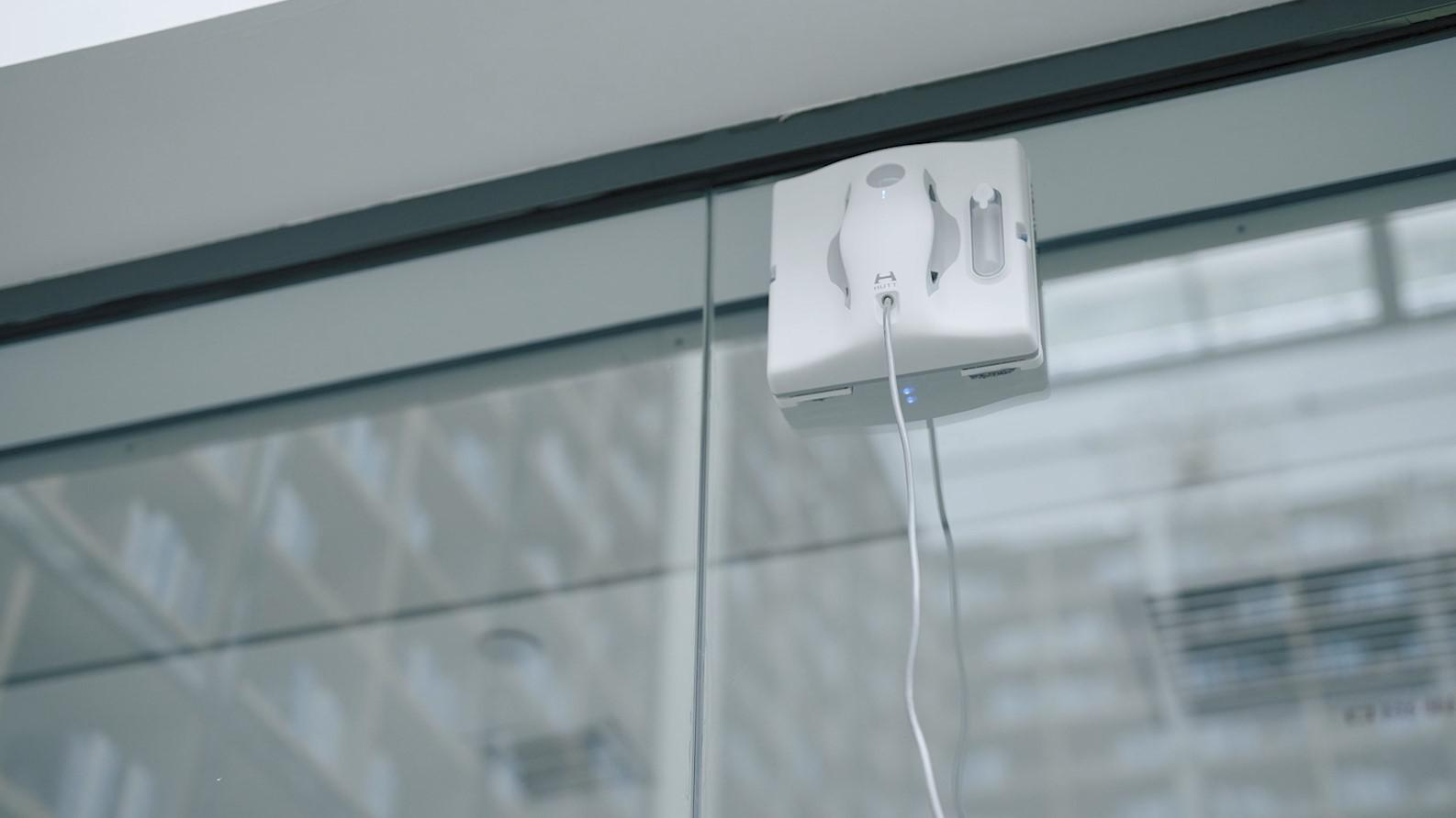 Ein Fensterputzroboter an einem Fenster mit Netzkabel.