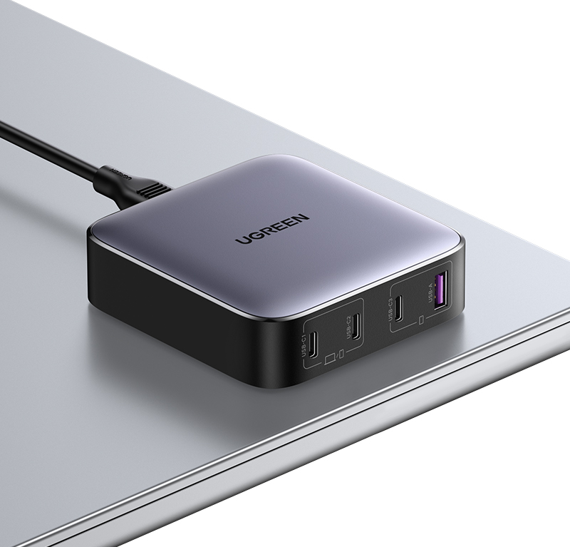 Ein grauer UGREEN-Netzadapter mit USB-Anschlüssen auf einer metallischen Oberfläche.