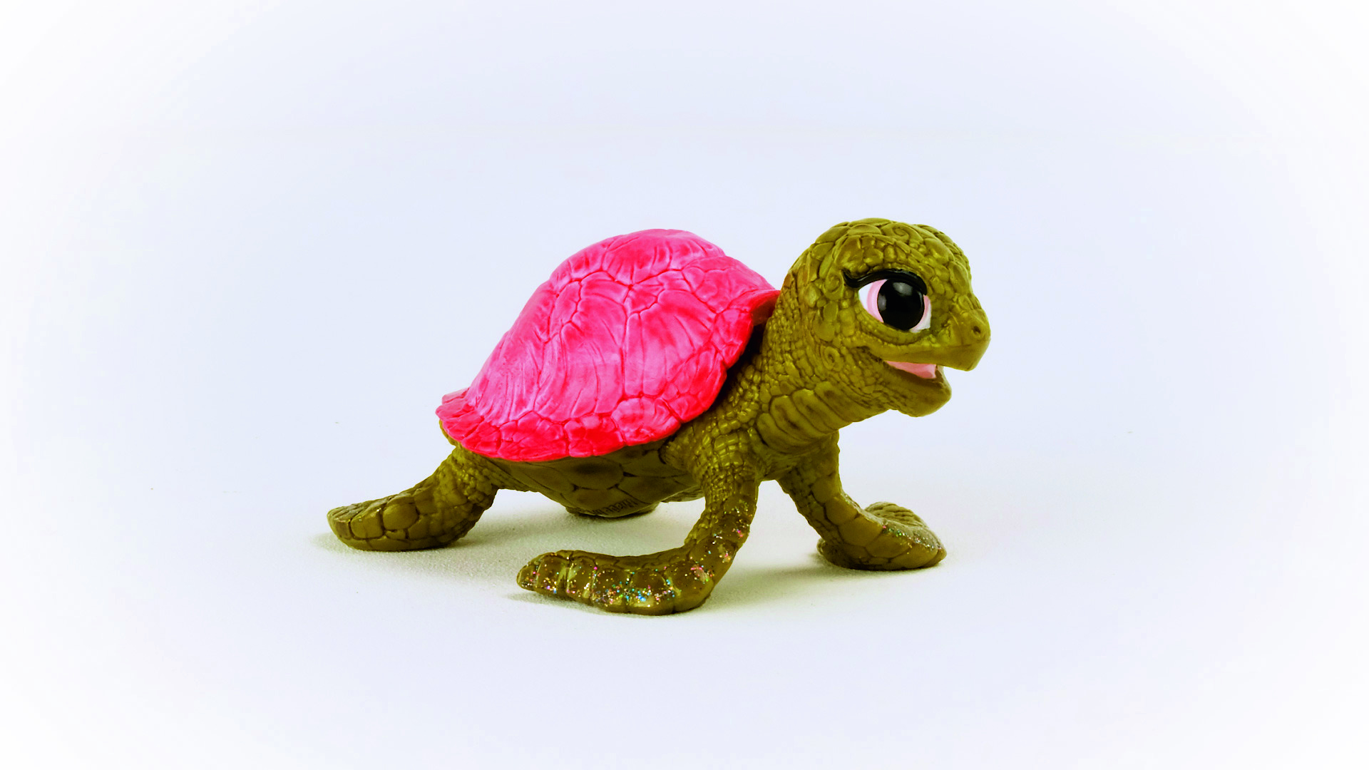 Grüne und rosa Spielzeugschildkröte auf weißem Hintergrund.