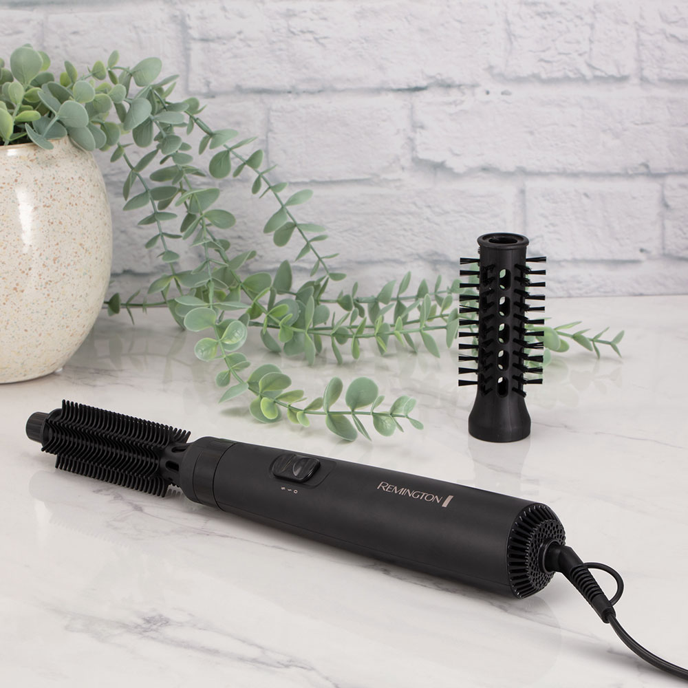 Remington-Haarstyler und zwei Aufsätze auf Marmoroberfläche, mit einer Pflanze im Hintergrund.