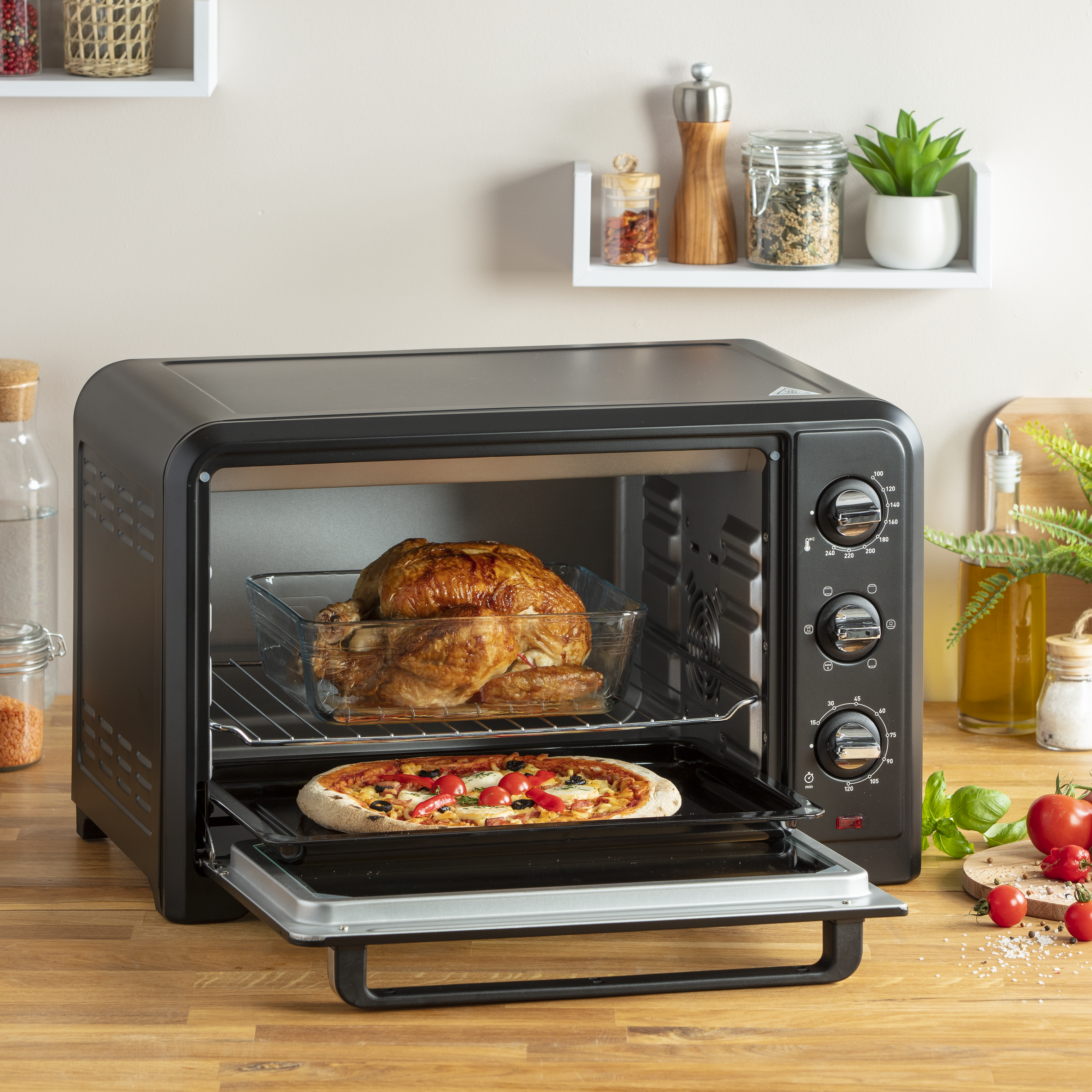 Un horno con puerta de vidrio, pizza en la rejilla inferior y un pollo en la rejilla superior.