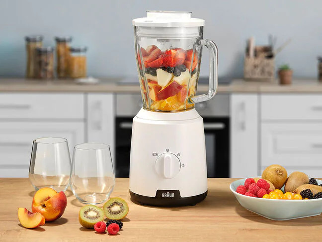 A white blender with fruits inside, set on a wooden table.