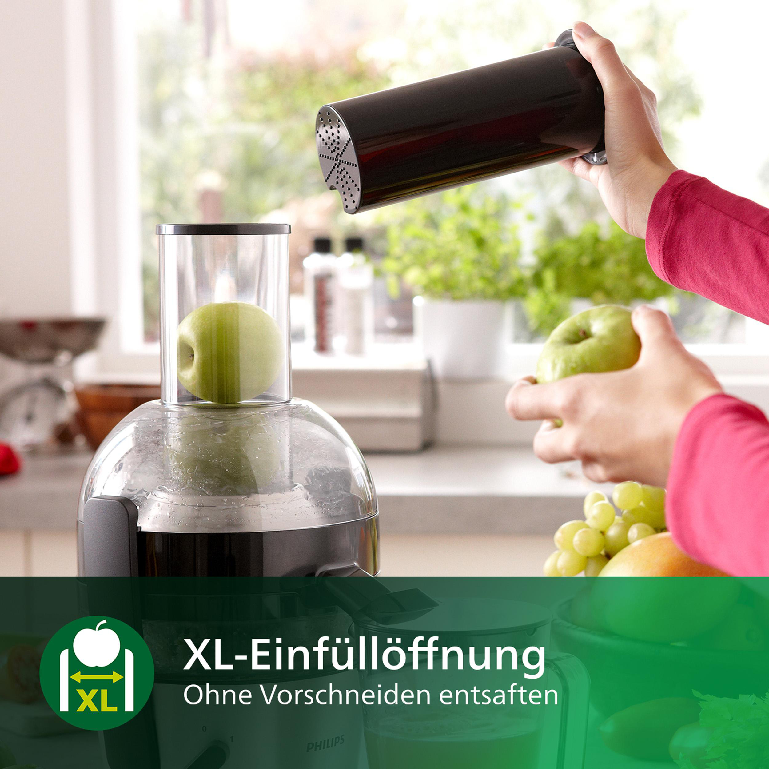 Eine Person benutzt einen Entsafter. Grüner Apfel wird hineingelegt. Ein weiterer Apfel und Trauben auf der Theke.