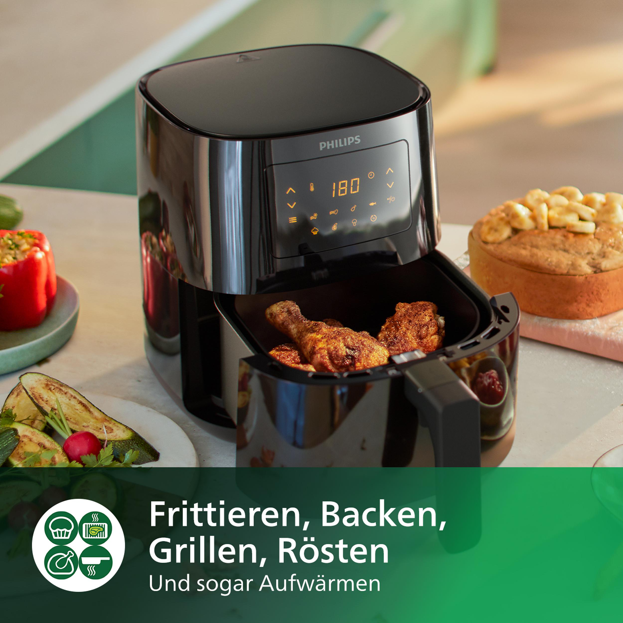 Heißluftfritteuse mit gebratenem Hähnchen und Gemüse. Andere Speisen stehen auf der Theke.