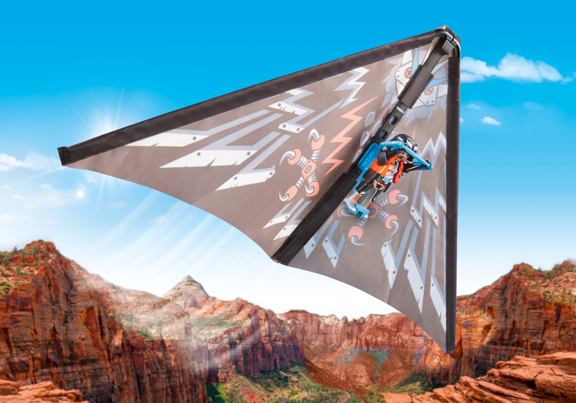 Ein blaues Spielzeugflugzeug fliegt über einen Canyon. Das Flugzeug ist an einer Drachen befestigt.