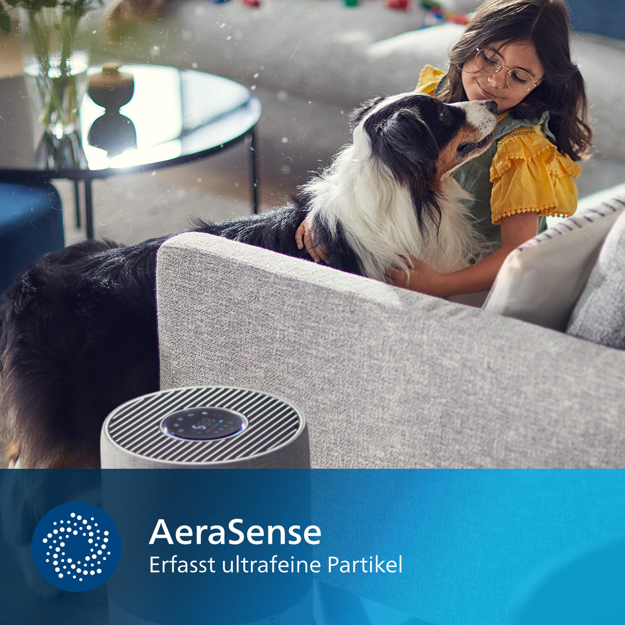 Mädchen umarmt Hund auf grauem Sofa neben Luftreiniger.