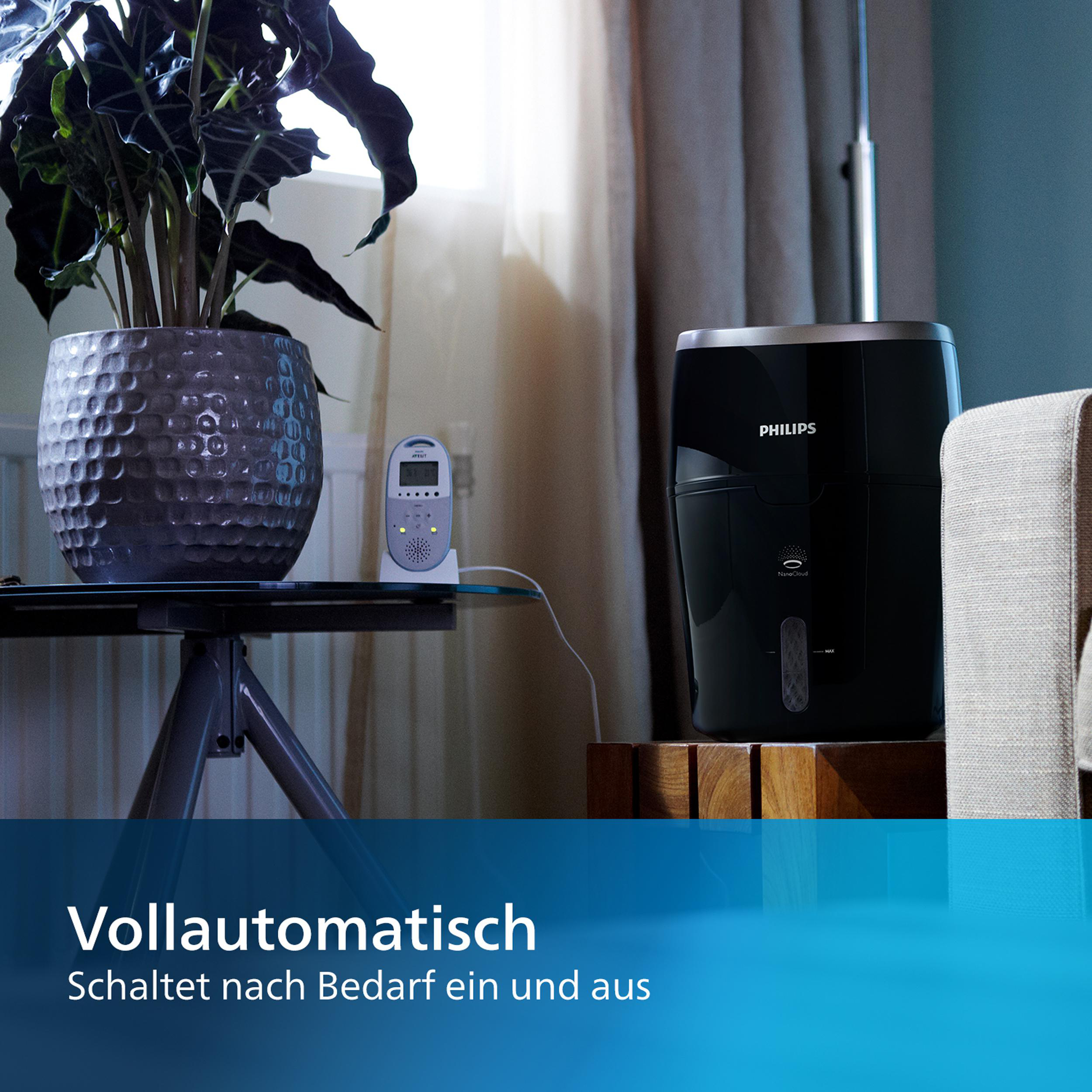 Luftbefeuchter mit einer Pflanze auf einem Tisch und einem Babyphone. Text auf Deutsch.