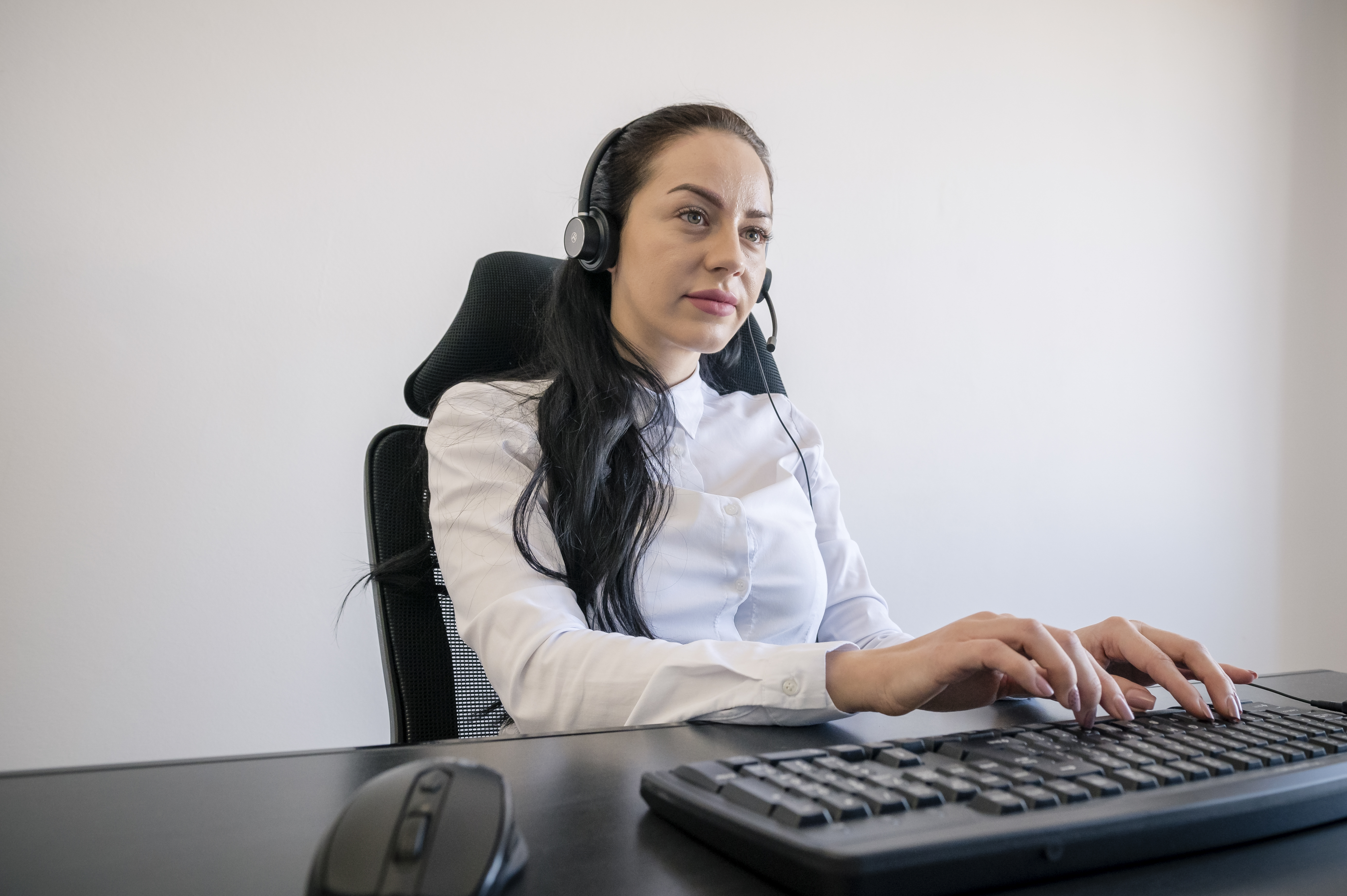 Kobieta z zestawem słuchawkowym pracuje przy biurku, pisząc na klawiaturze.