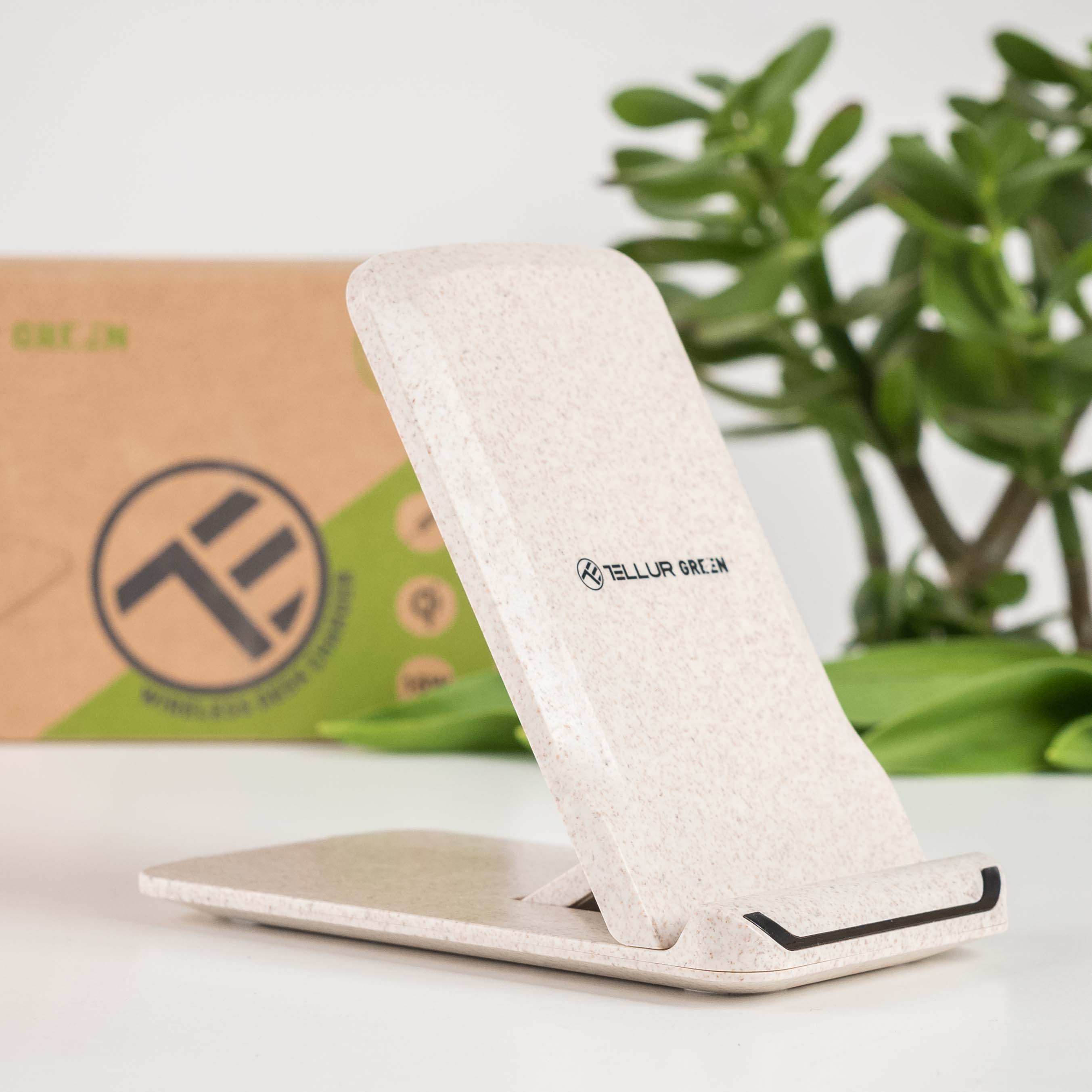 Ein beiges kabelloses Ladegerät, angewinkelt, mit einer grünen Pflanze und einer Box mit dem Logo 'TELLUR GREEN' im Hintergrund.