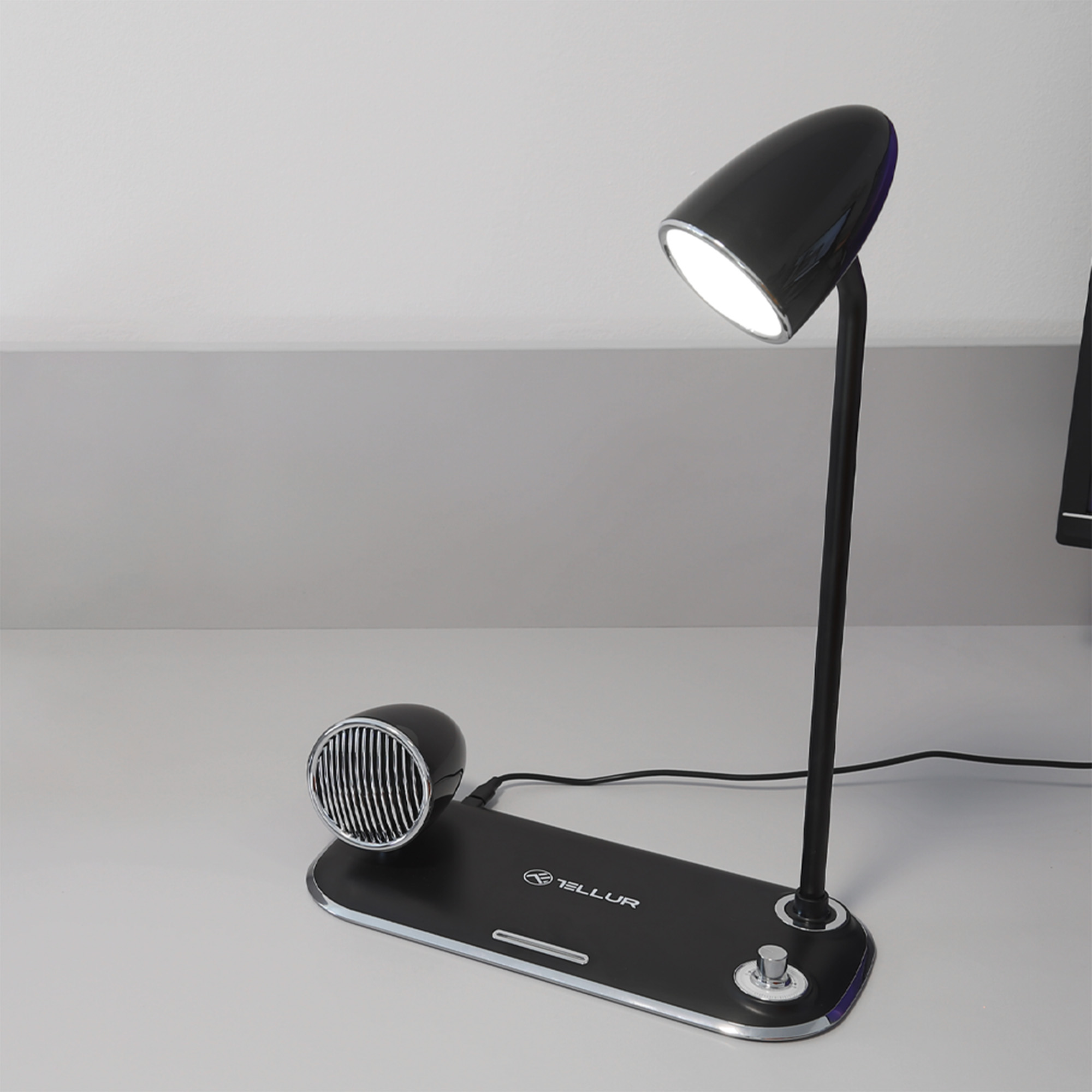 Czarna lampa biurkowa z zaokrągloną głowicą i wbudowanym głośnikiem na czarnej podstawie.