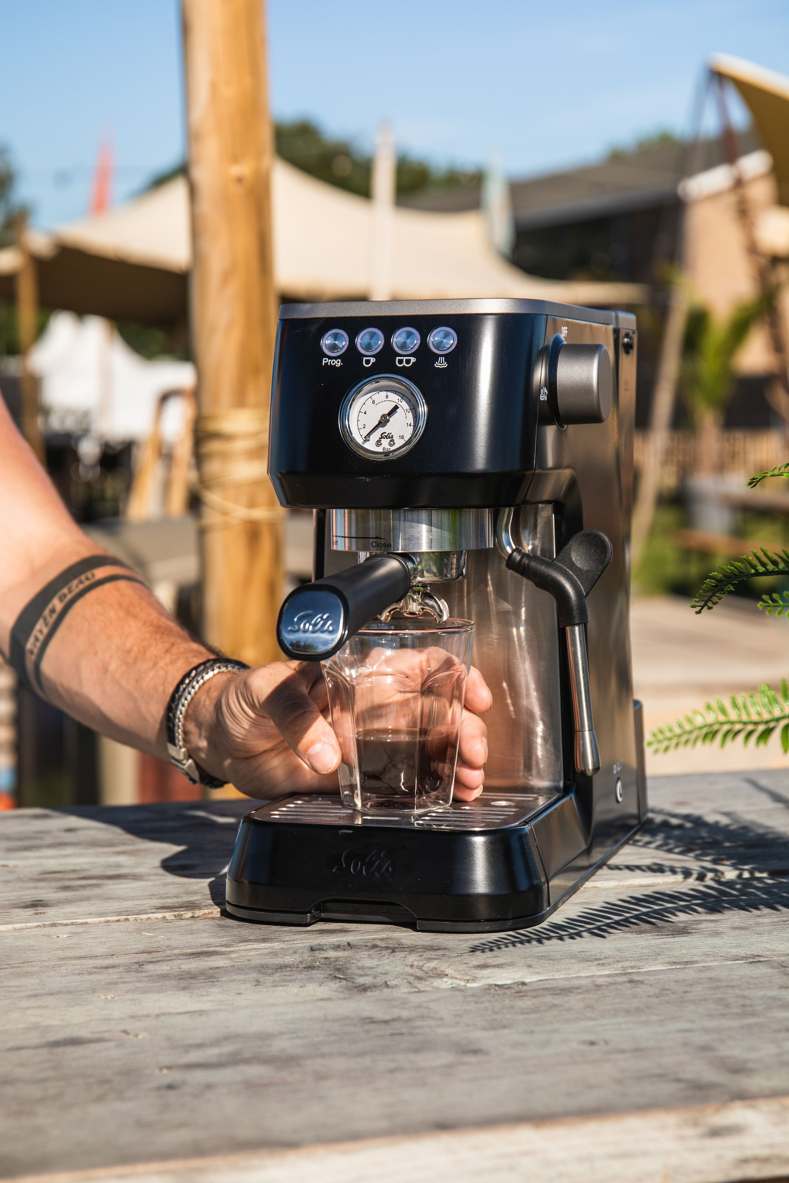 Espressomaschine mit Glas. Eine Hand hält das Glas. Hintergrund im Freien.