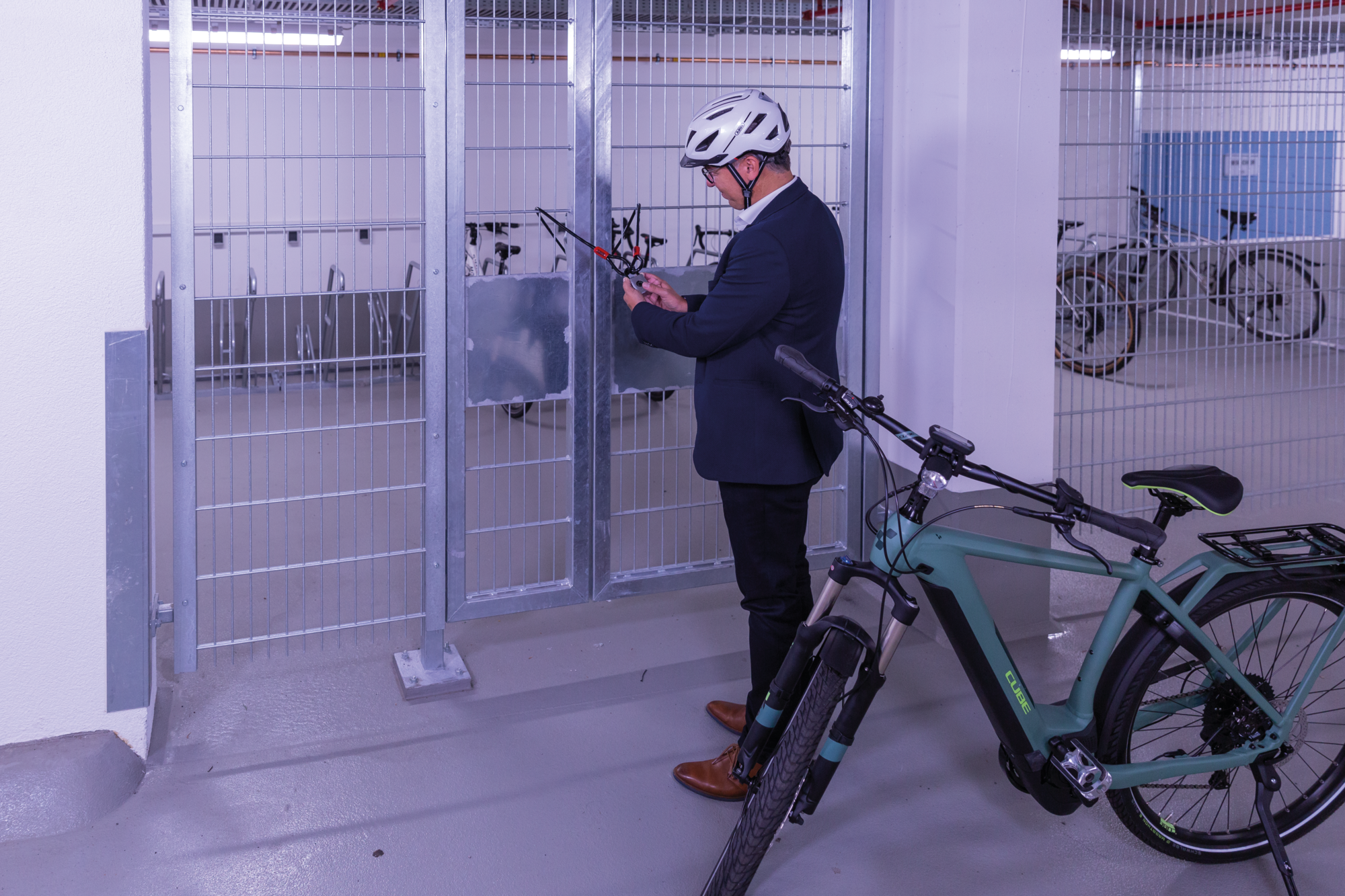 Mann in Anzug an E-Bike in Parkgarage. Er benutzt einen Schlüssel, um das Fahrrad zu verschließen. Andere Fahrräder im Hintergrund.