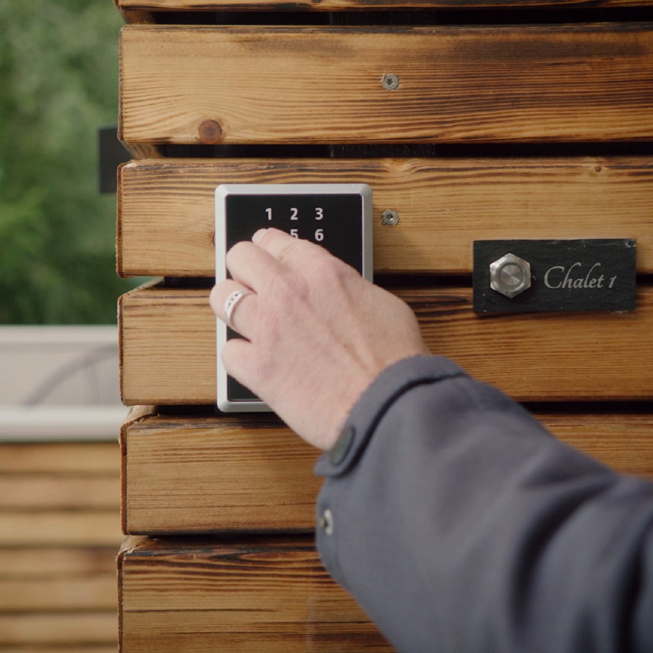 Hand gibt Code in eine Tastatur an einer Holzwand ein.