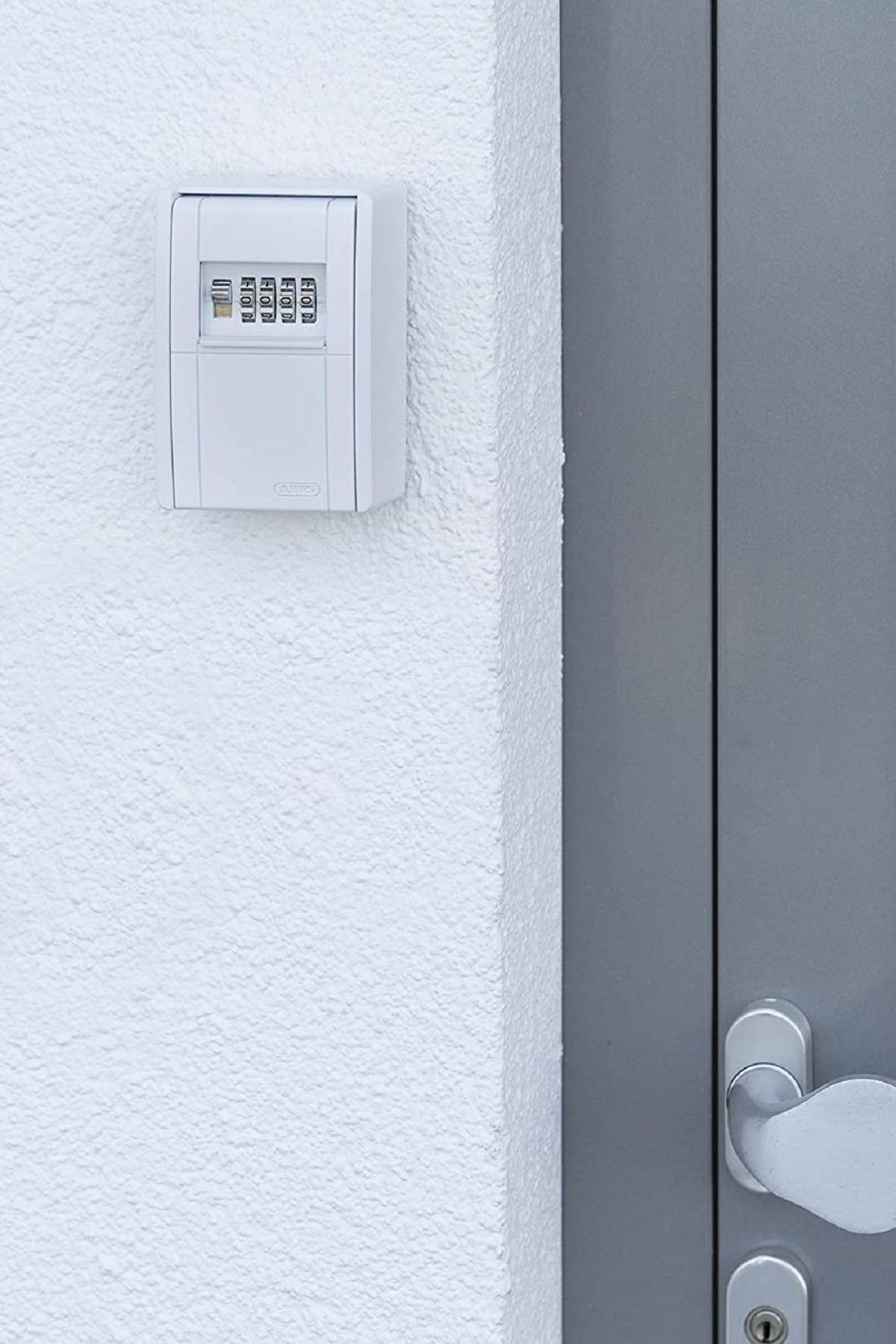 Ein weißes Tastatur-Sicherheitssystem an einer strukturierten weißen Wand neben einer grauen Tür angebracht.