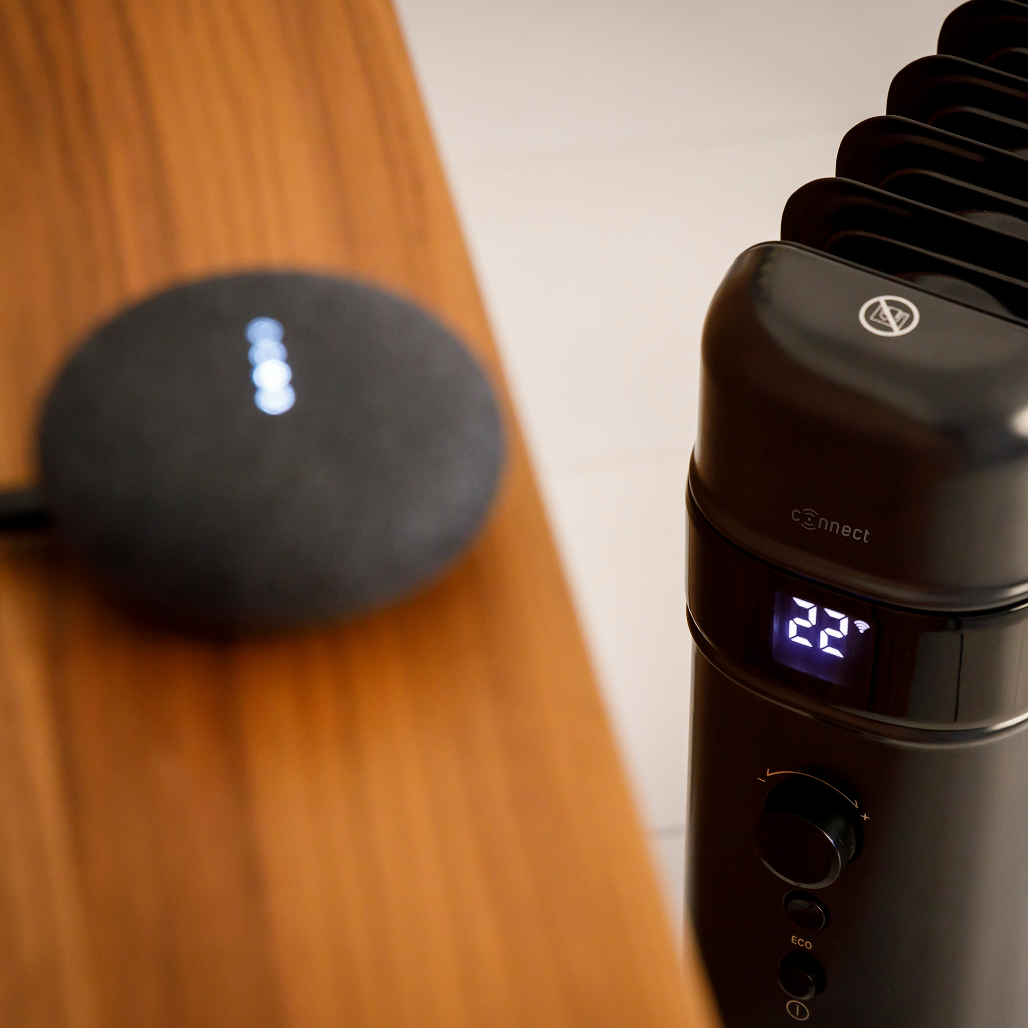 Schwarzer Google Nest Mini-Lautsprecher auf Holztisch, ein schwarzer Heizlüfter.