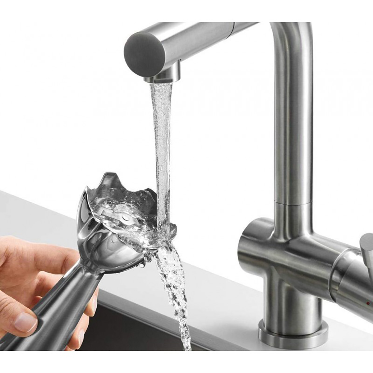 Dłoń trzymająca głowicę blendera pod kranem. Woda wypływa z kranu i głowicy blendera.