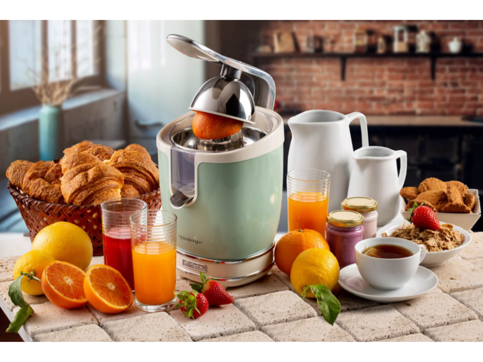 Scène de cuisine avec presse-agrumes, oranges, croissants, thé et autres articles de petit-déjeuner. Fond de mur en briques.